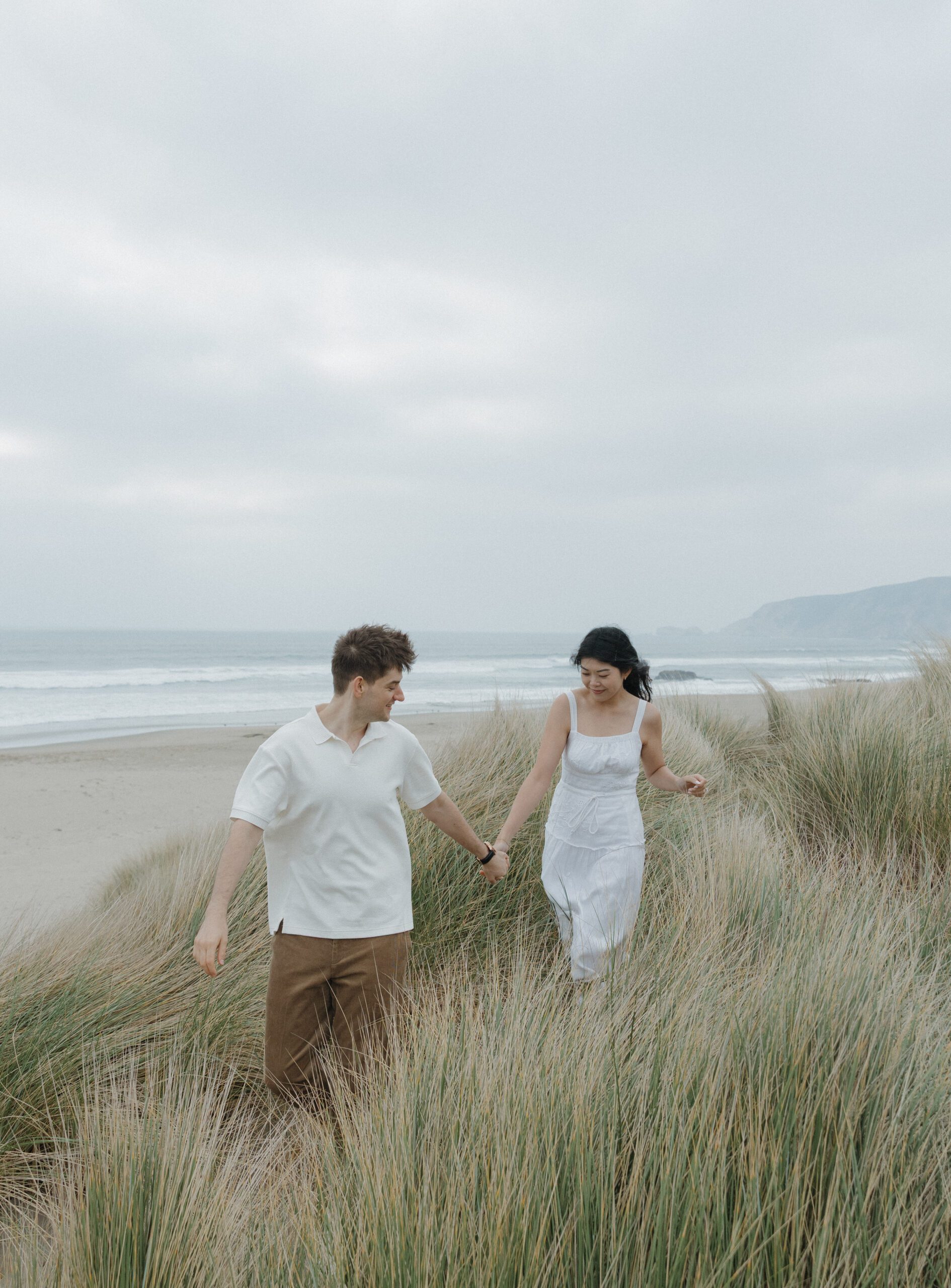 Couple walking through grassy fields during engagement photos