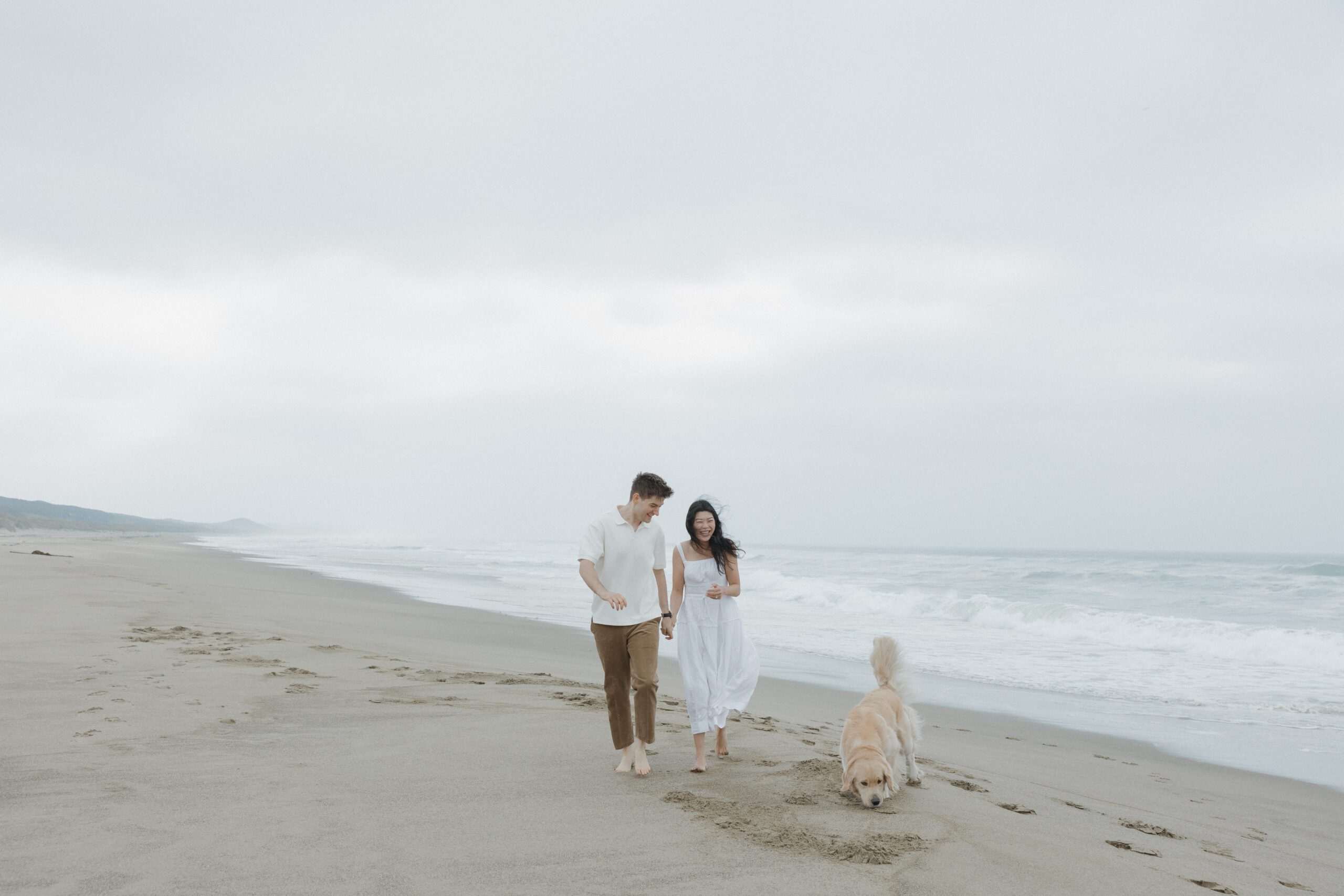A couple walking with their dog on the beach for engagement photos