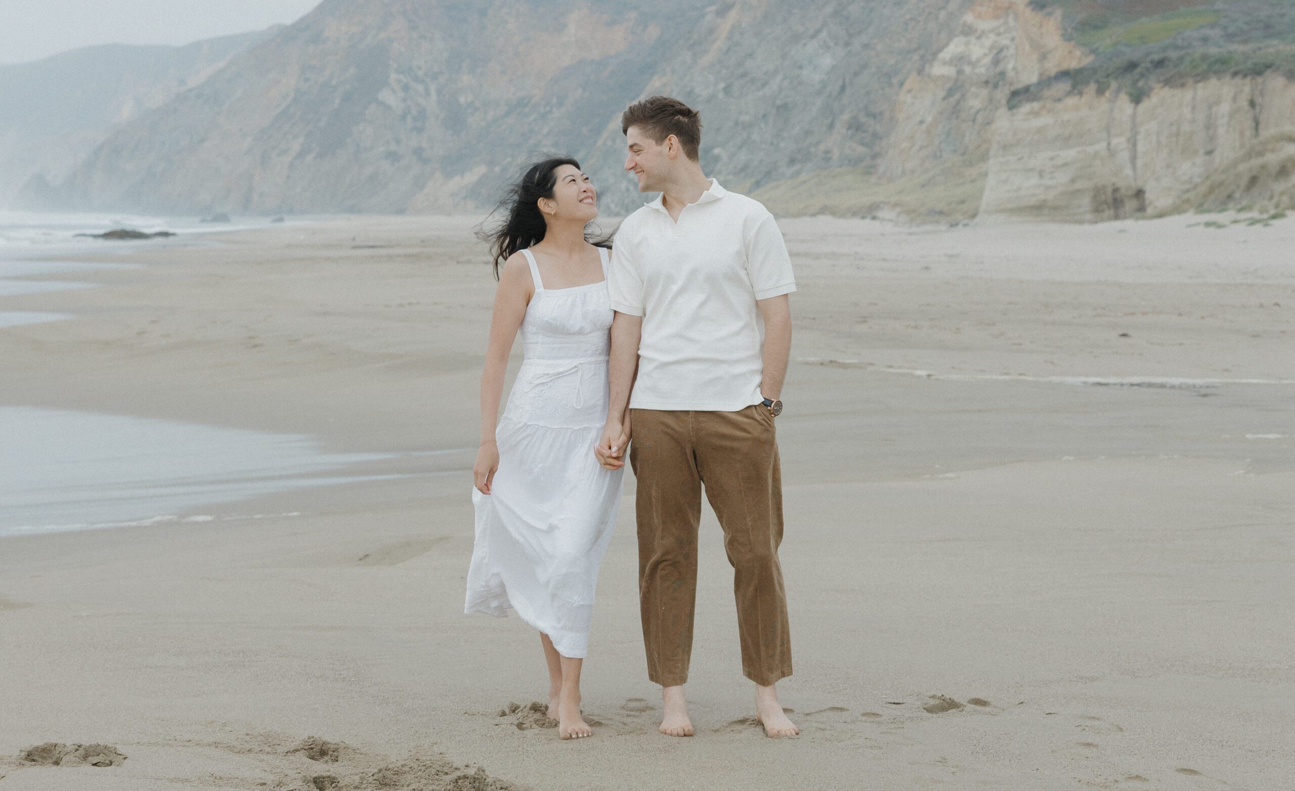 A couple smiling at each other on the beach during engagement photos