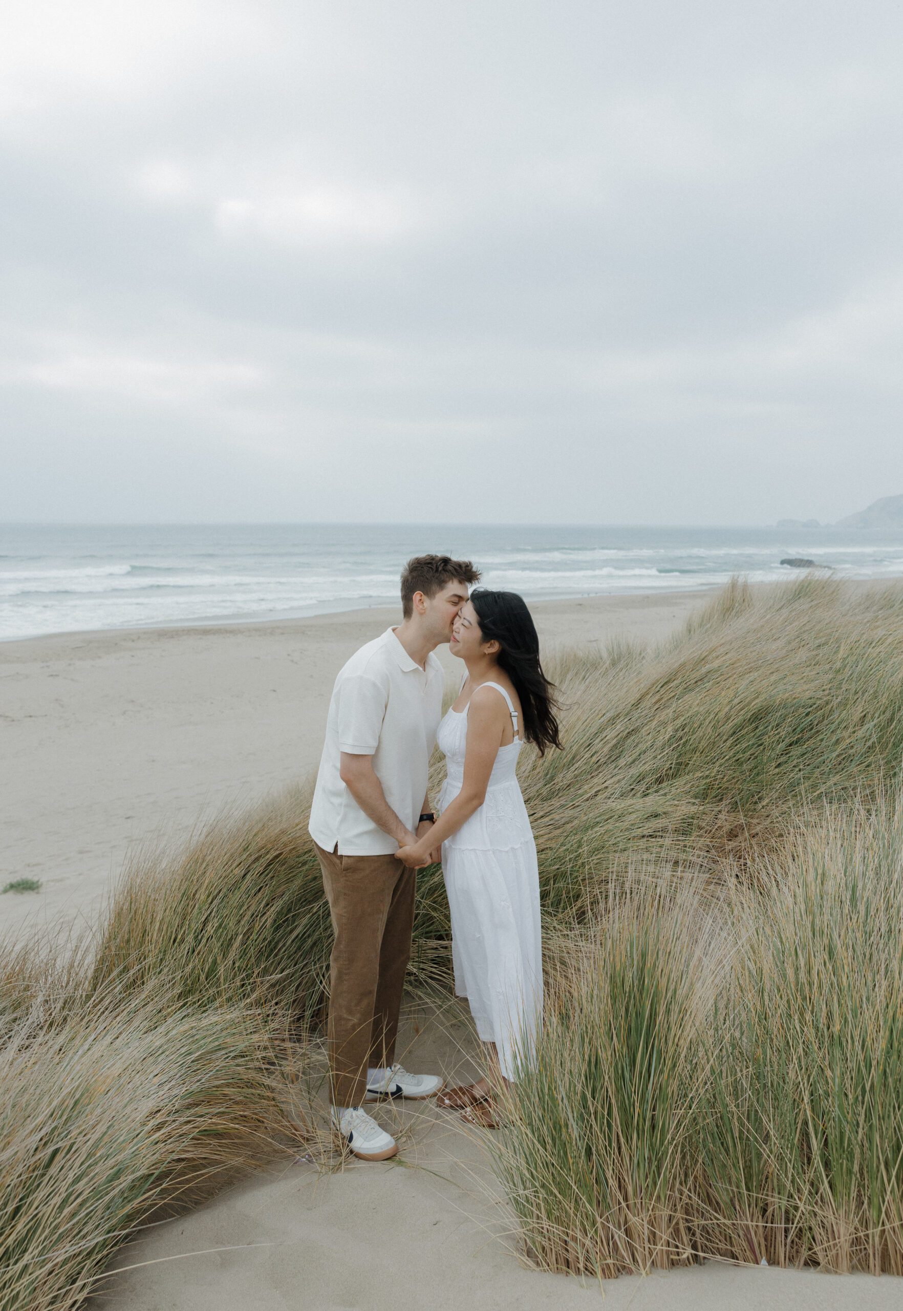 Guy kissing his fiancee on the cheek on the beach