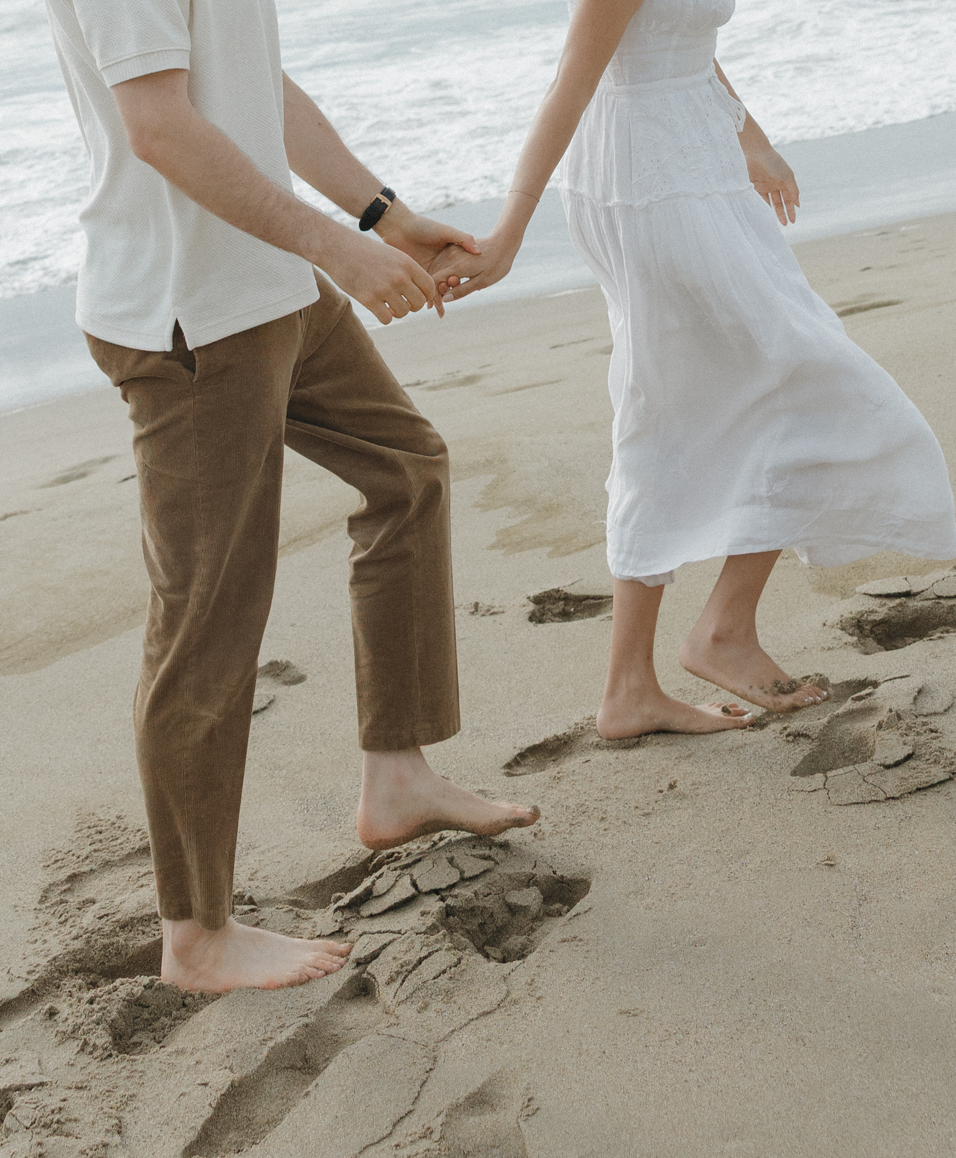 An editorial engagement photo of a couple walking on the beach