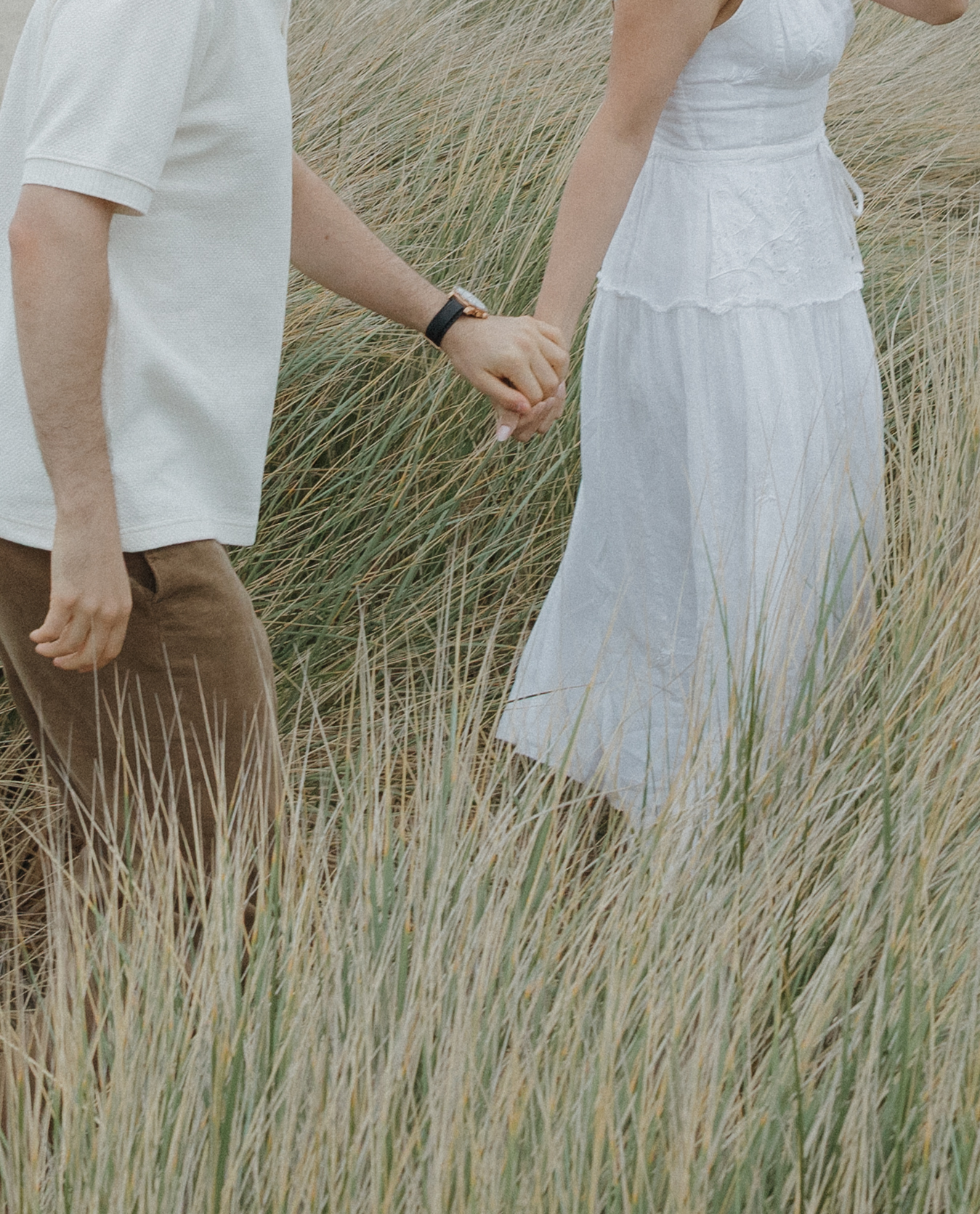 A couple walking through a grassy field during their engagement photoshoot
