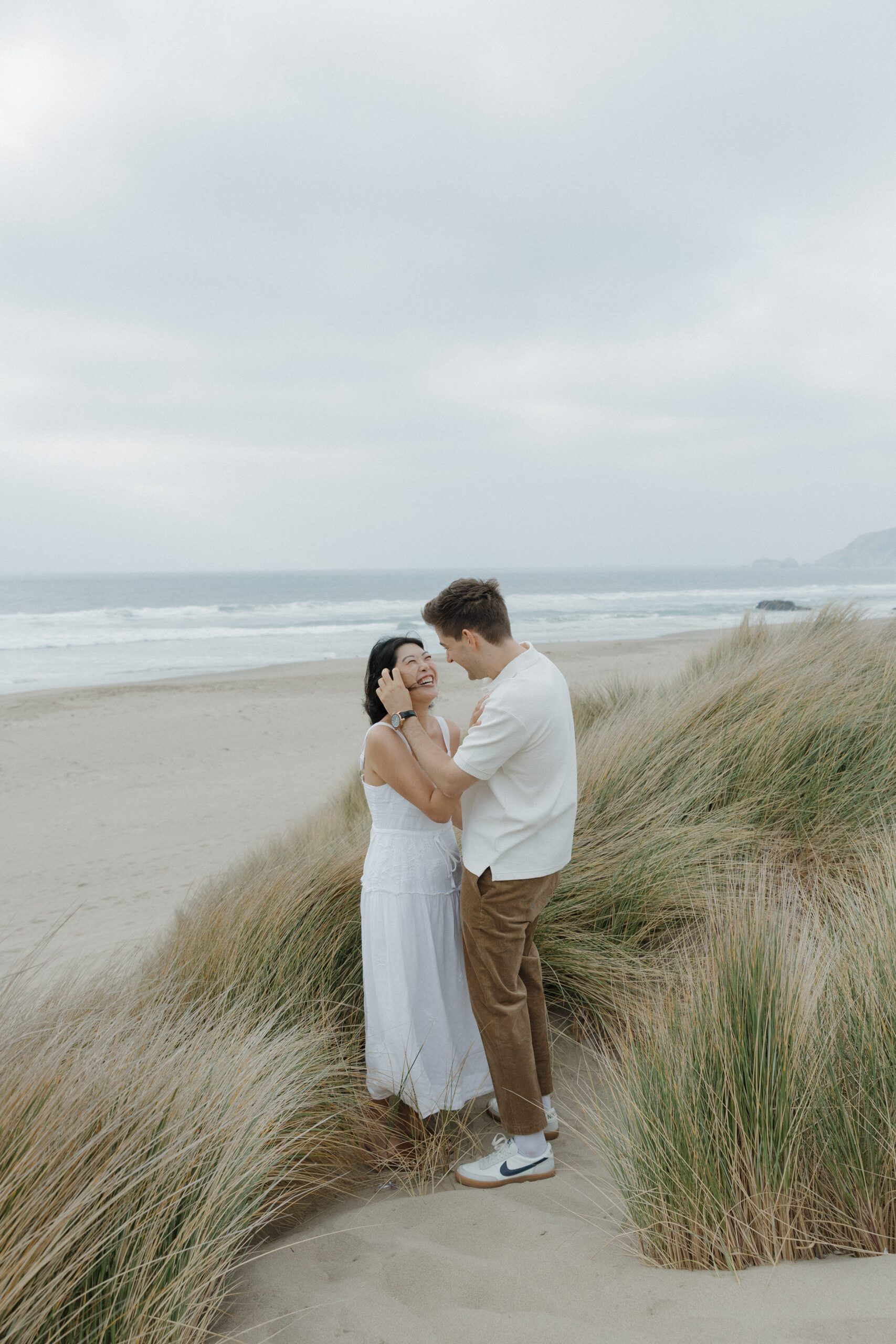 Man tucking hair behind his fiancees ear during beach engagement photoshoot