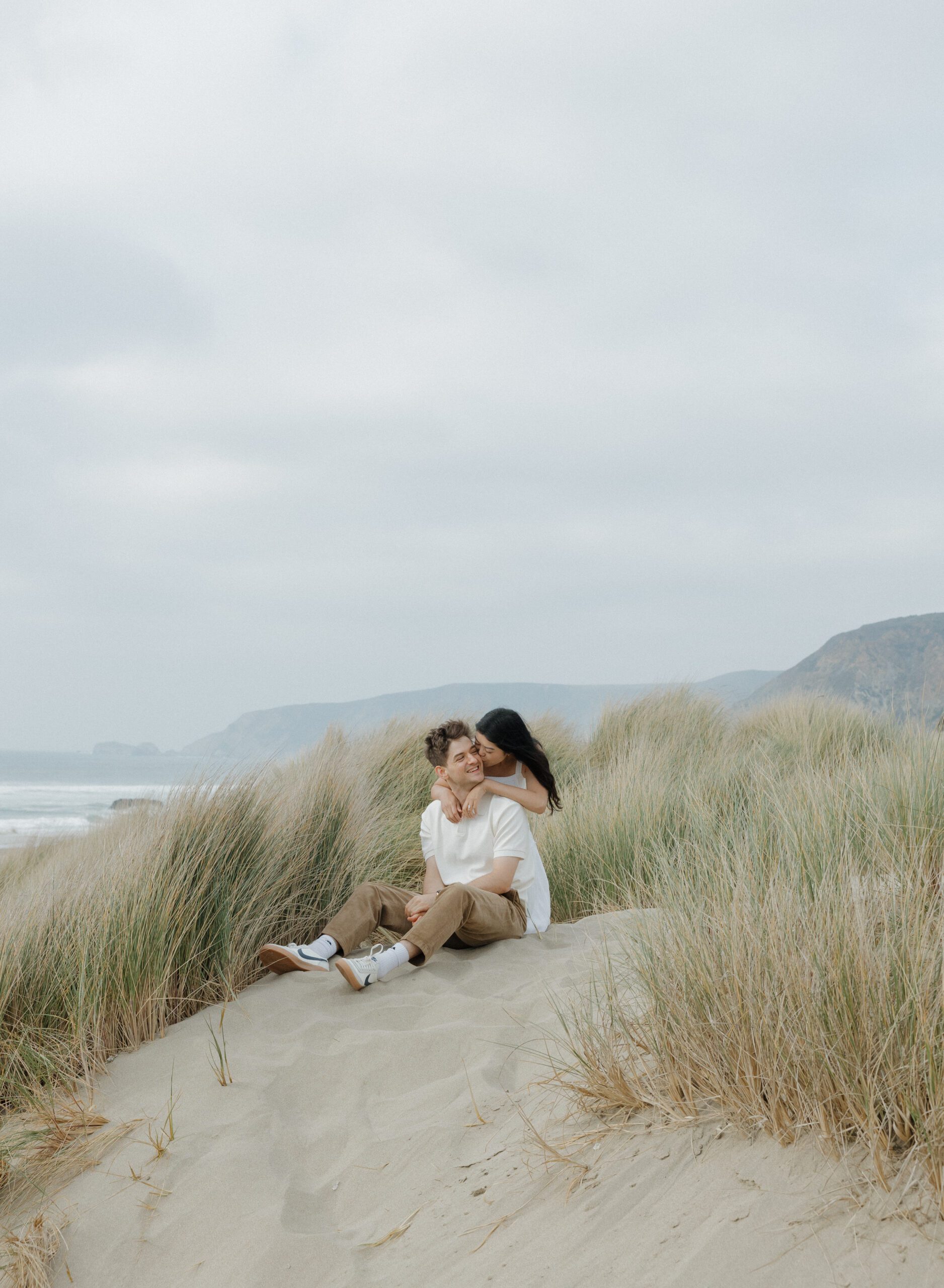 A girl hugging her fiancé from behind on a sand dune