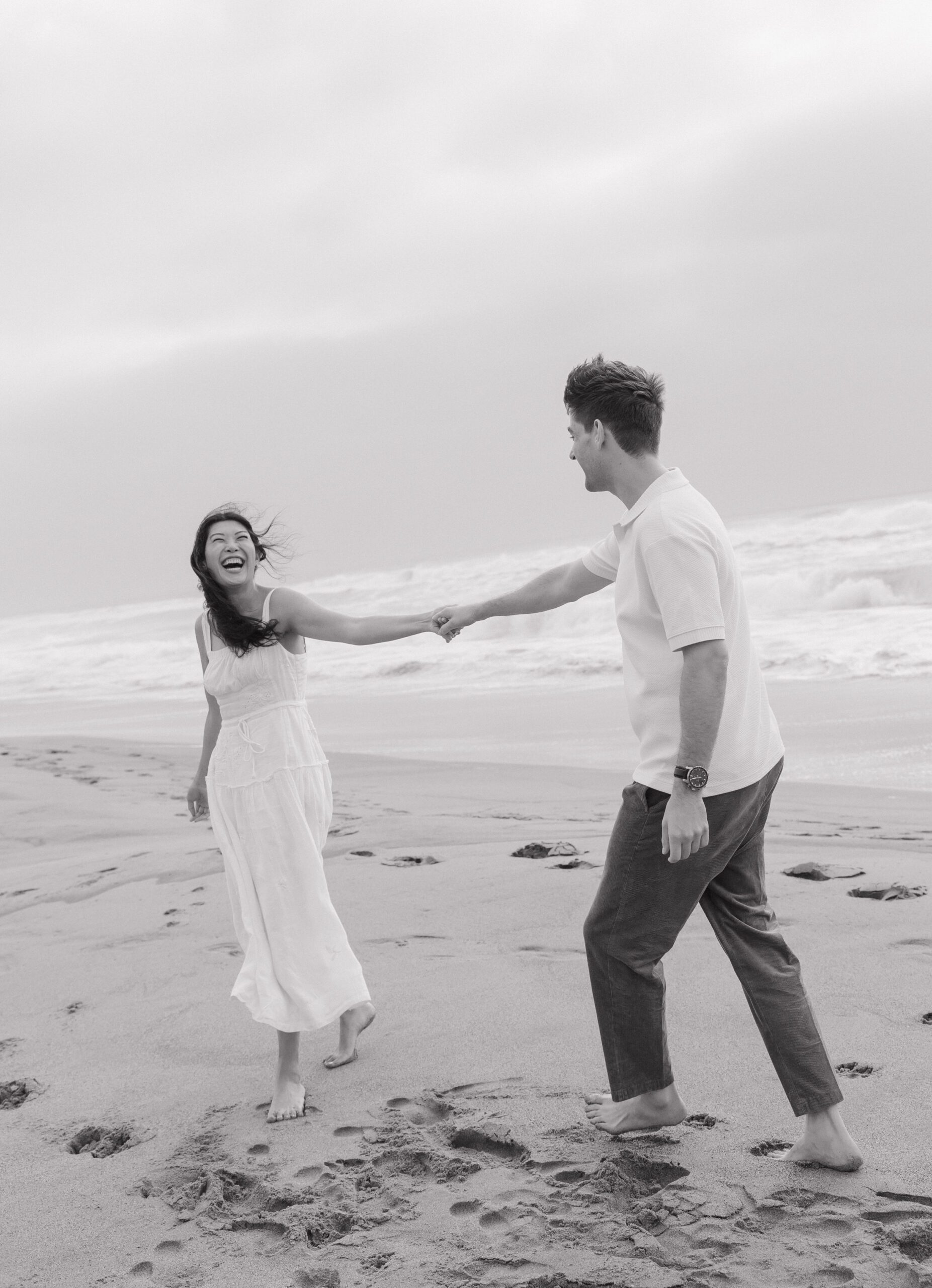 Couple laughing while walking on the beach during engagement photos