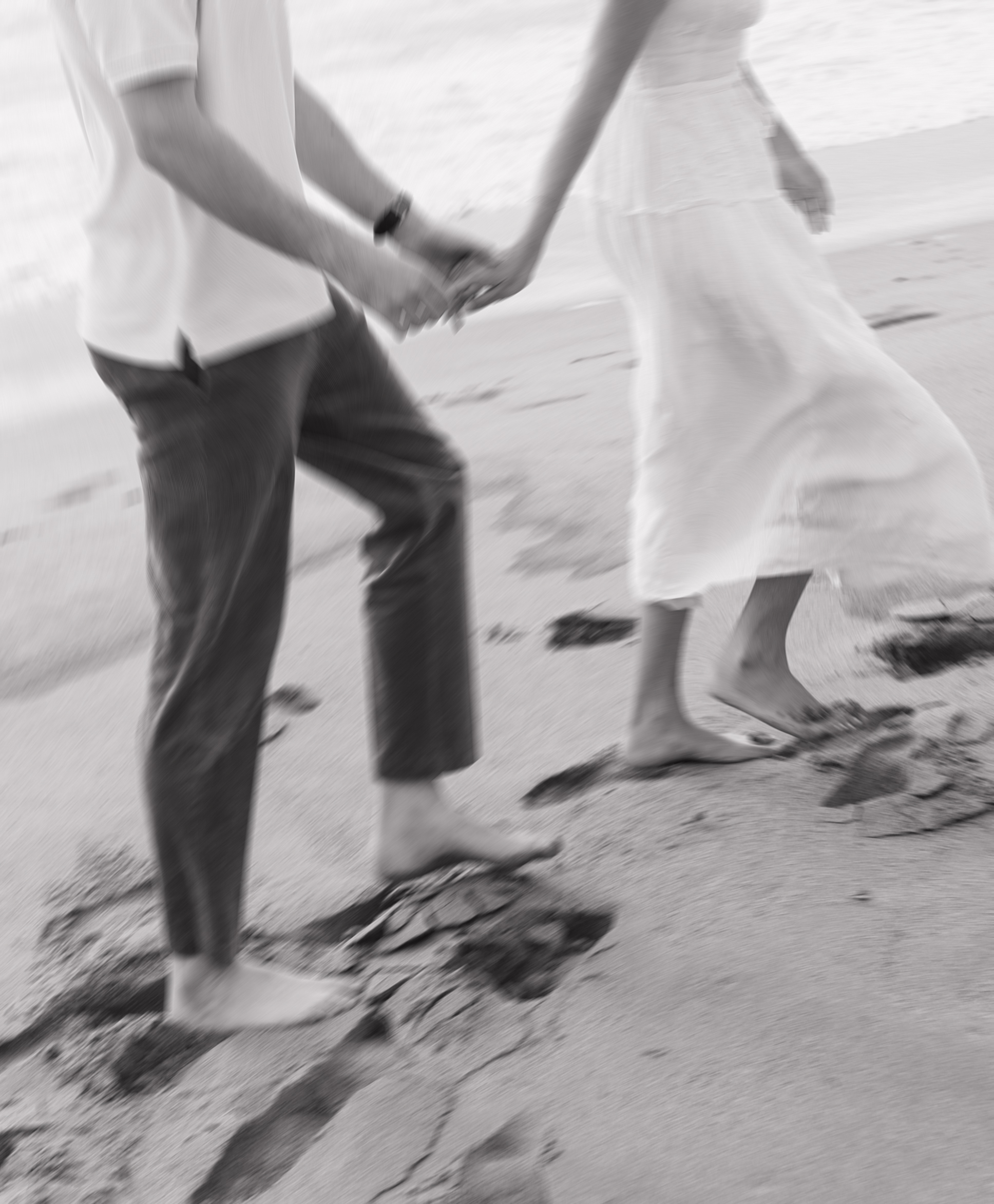 Black and white blurry engagement photo of couple holding hands walking on the beach