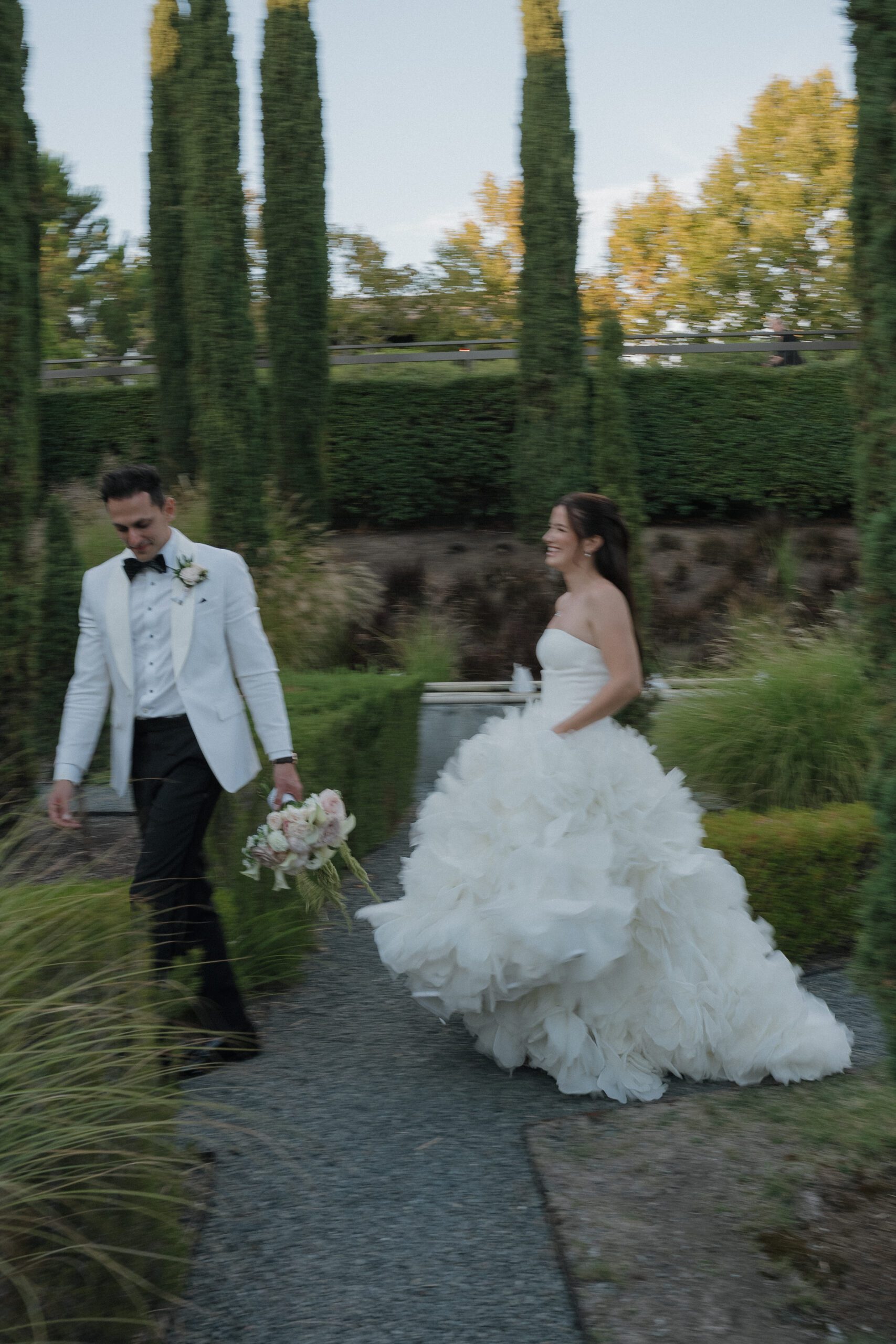 Blurry wedding photo of bride and groom walking through gardens