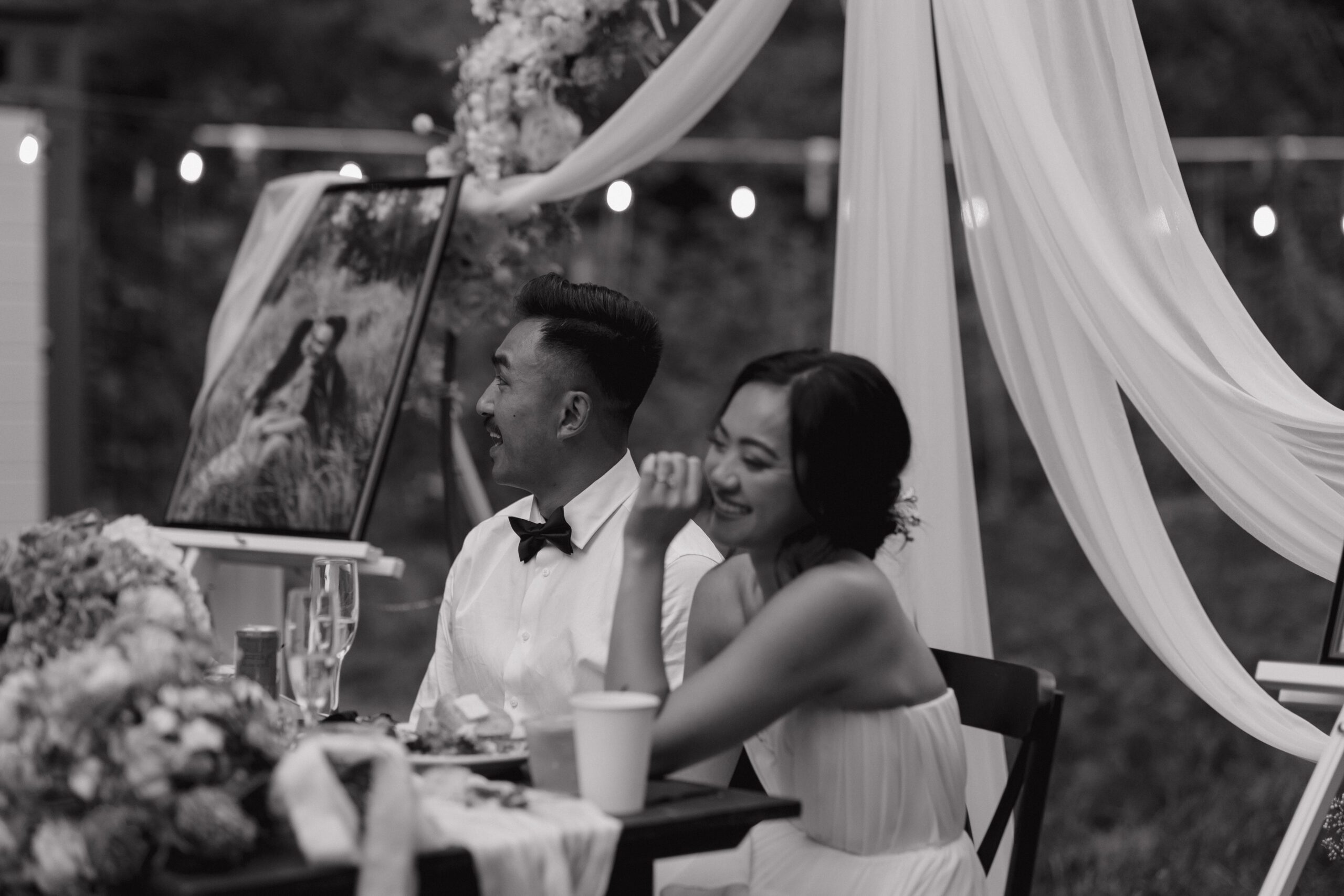 A black and white photo of a couple laughing during wedding toasts at an intimate wedding