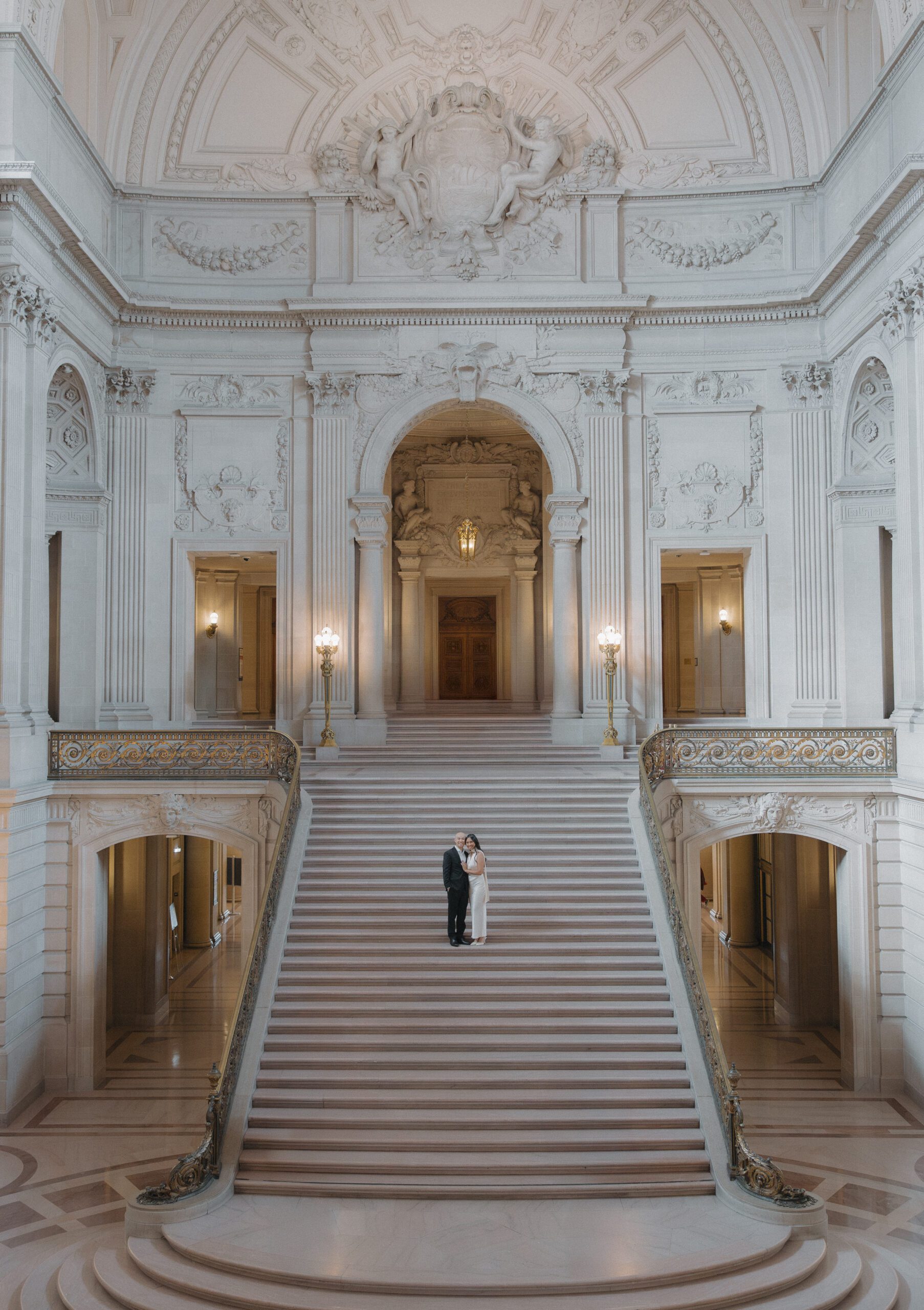 A couple posing for engagement photos on the grand staircase in San Francisco city hall
