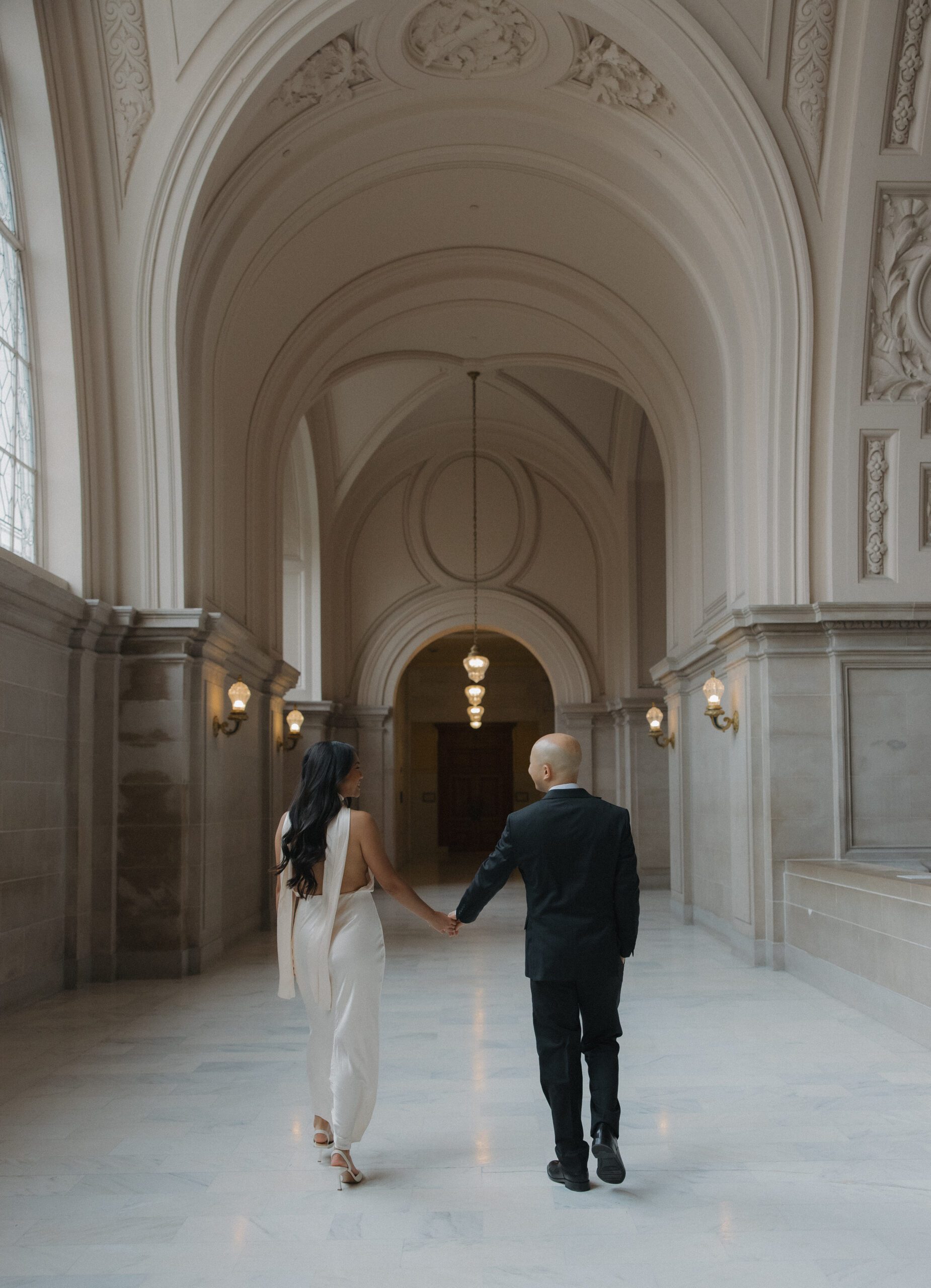 A couple walking through the fourth floor hallways at San Francisco city hall for their engagement photoshoot