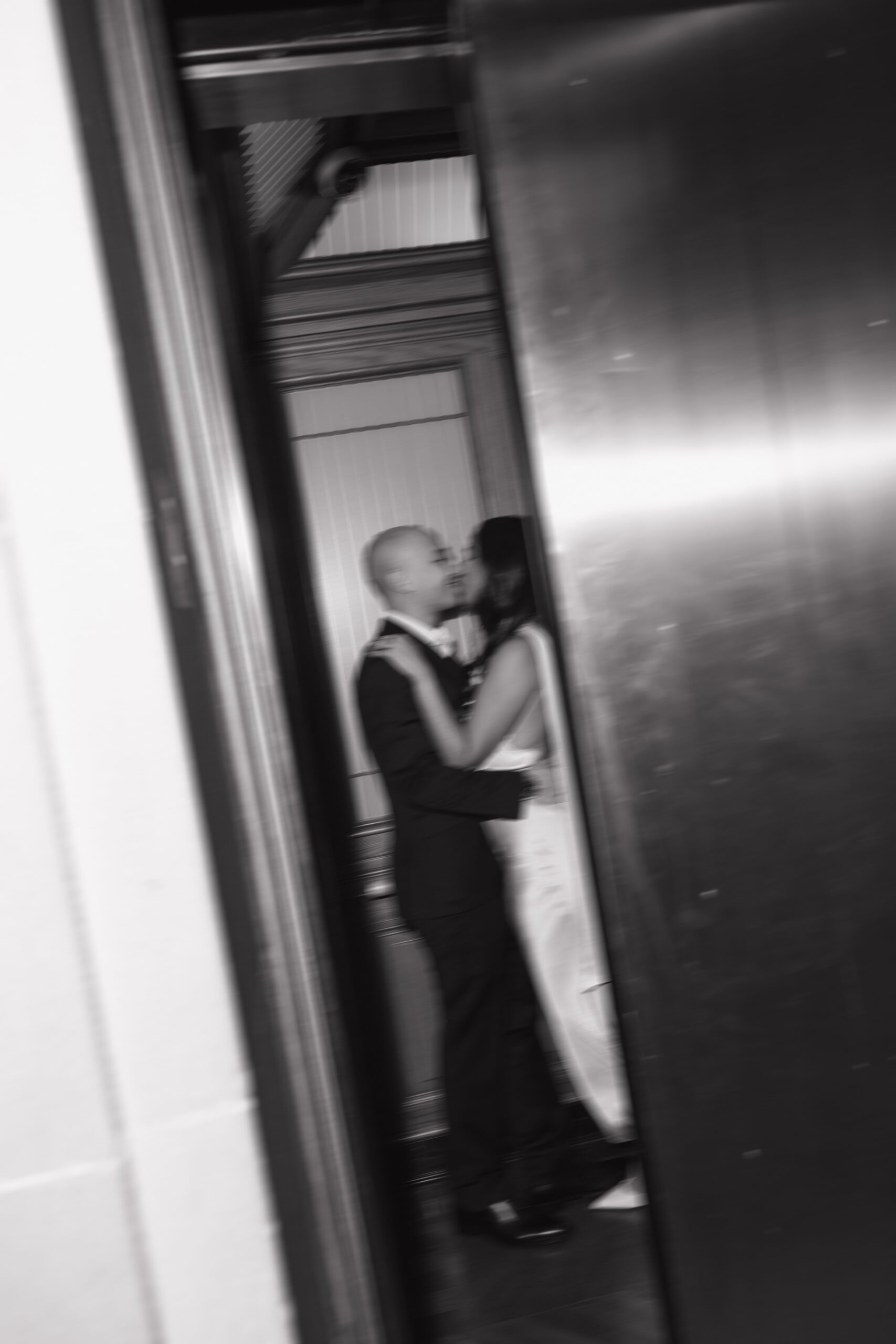 A black and white blurry photo of couple kissing while the elevator door closes