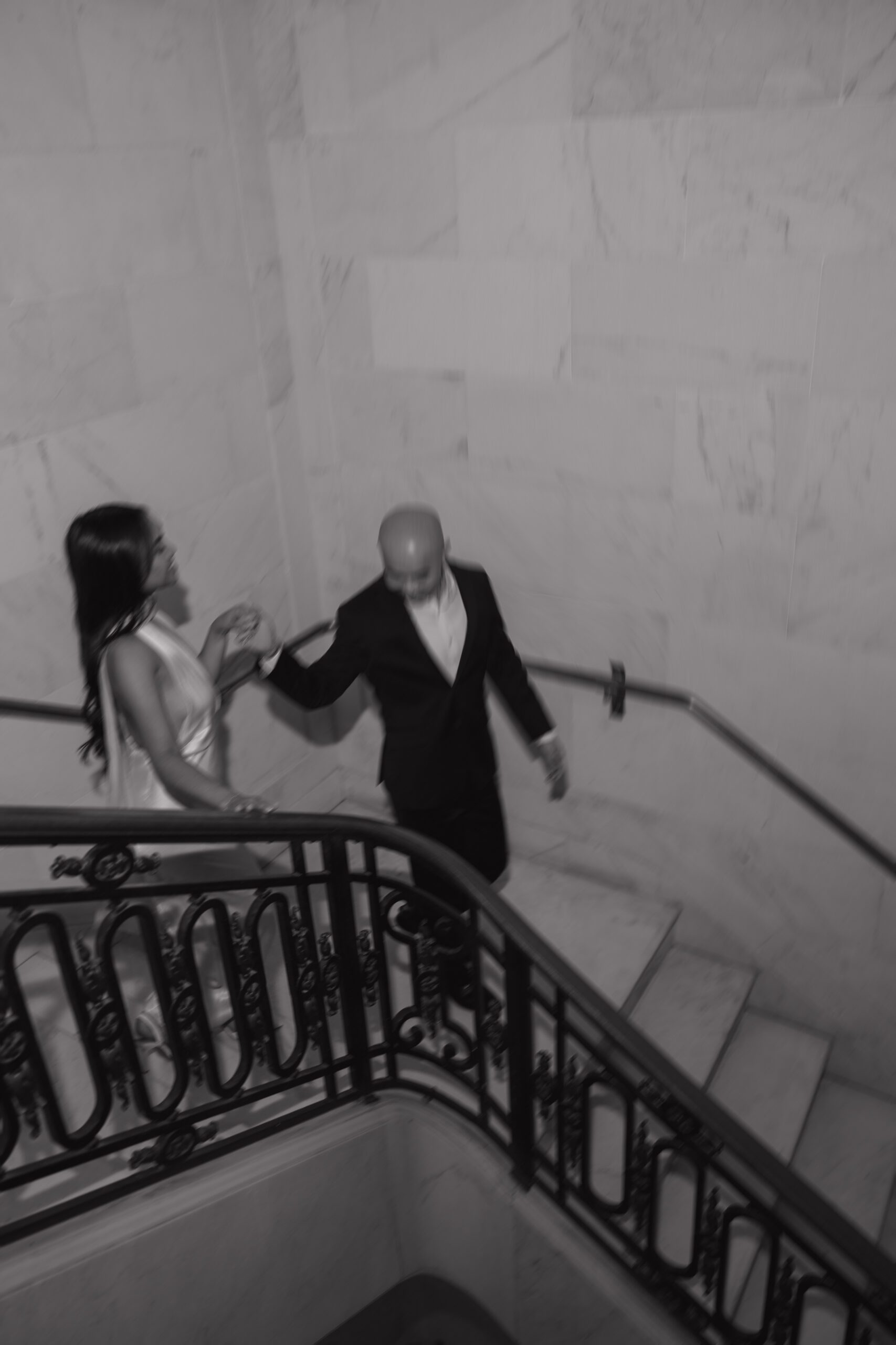 A black and white blurry photo of couple walking down marble stairs