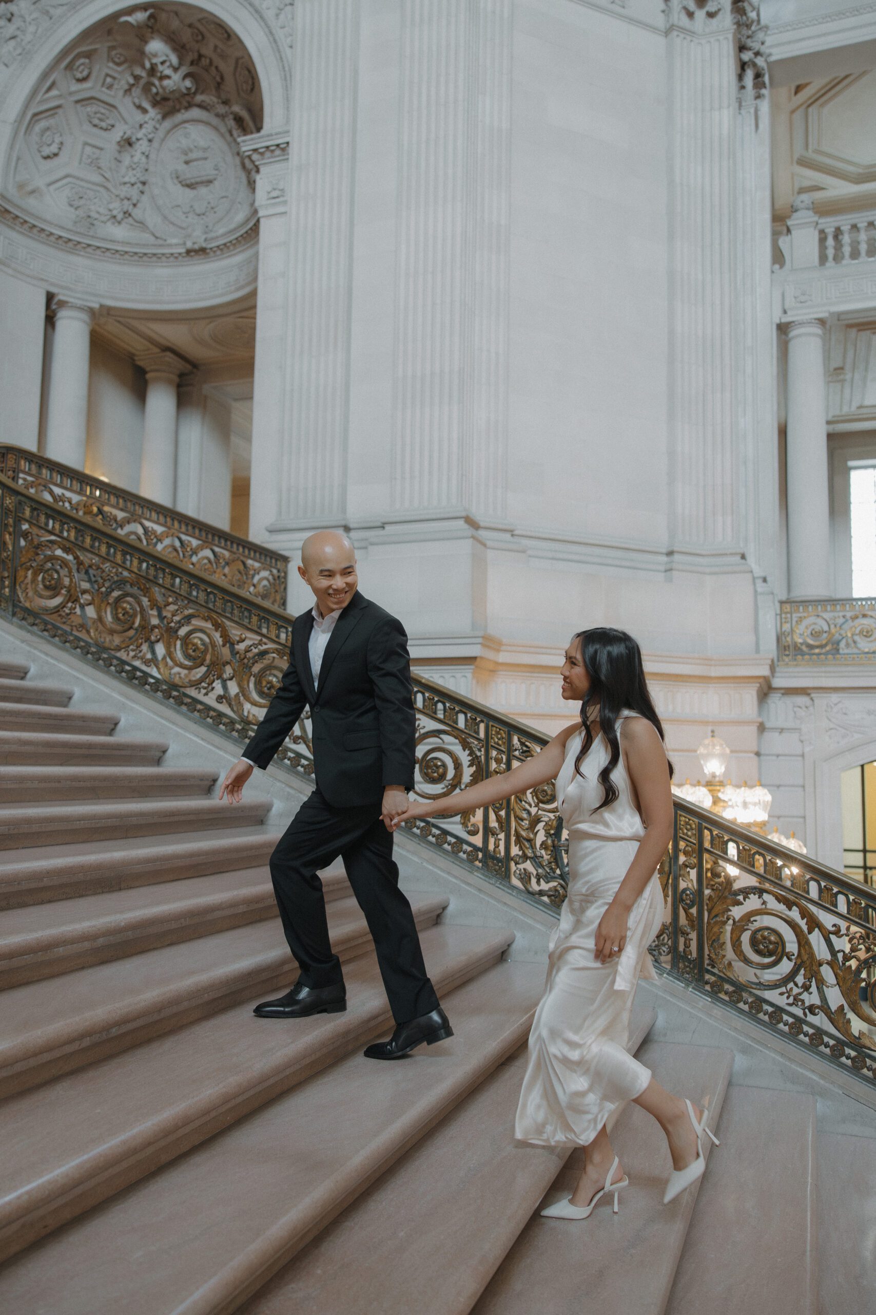 A couple holding hands walking up the grand staircase during San Francisco City Hall photos
