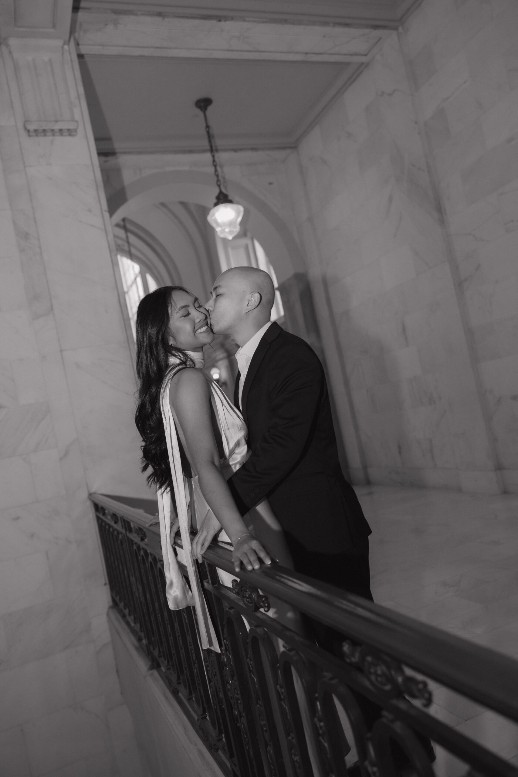 A man kissing his fiancee on the cheek during San Francisco City Hall photos for their engagement photoshoot 