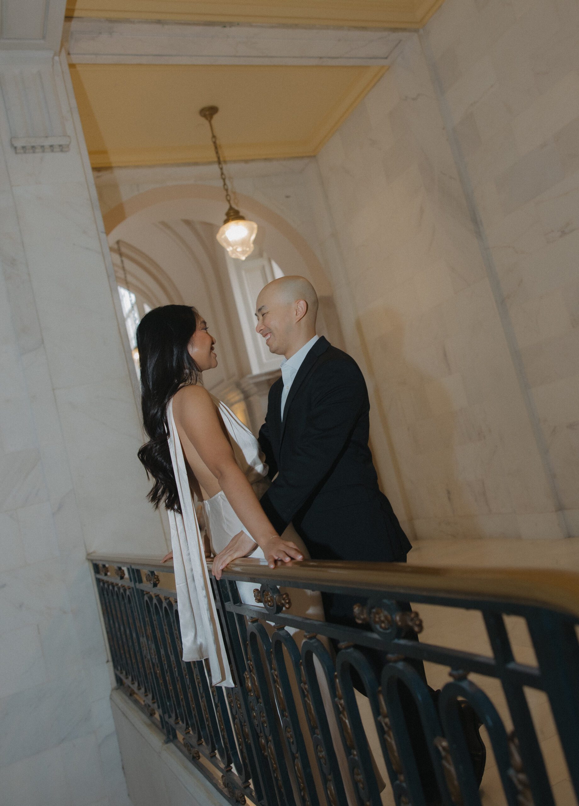A couple leaning against a balcony at City Hall during their engagement photoshoot 