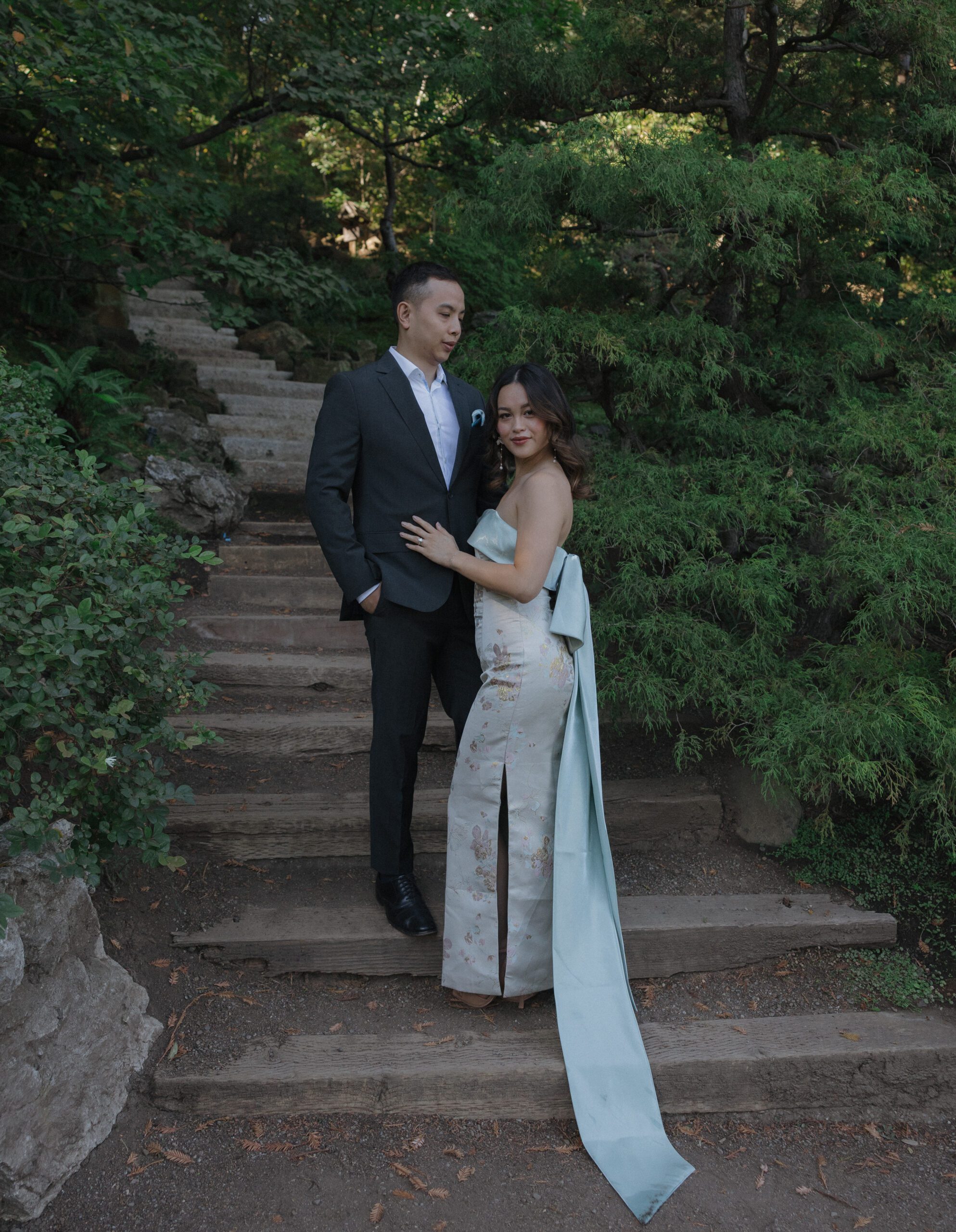 A couple posing for engagement photos on stairs in a forest