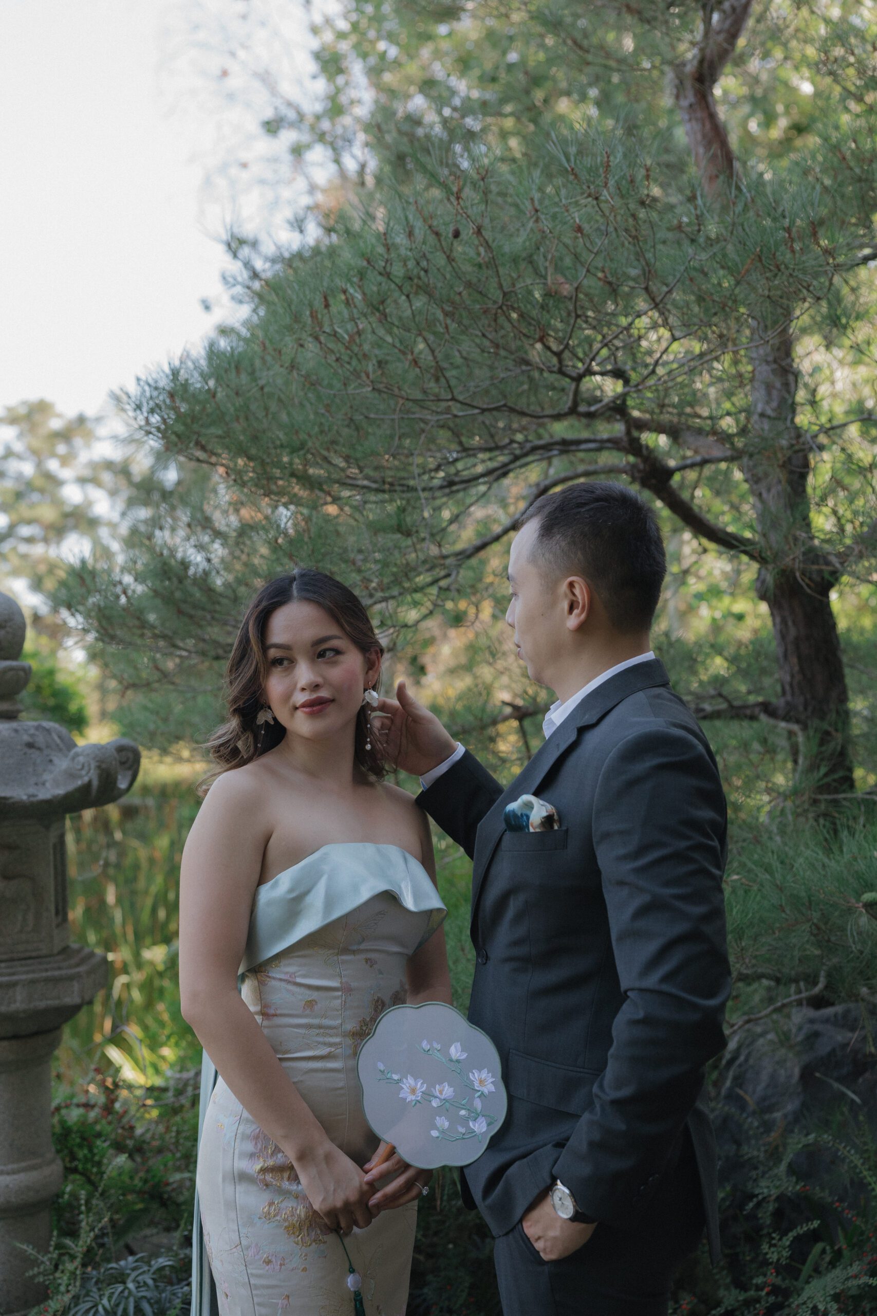 A woman wearing a jacquard dress with floral earrings and a floral fan for her engagement photos