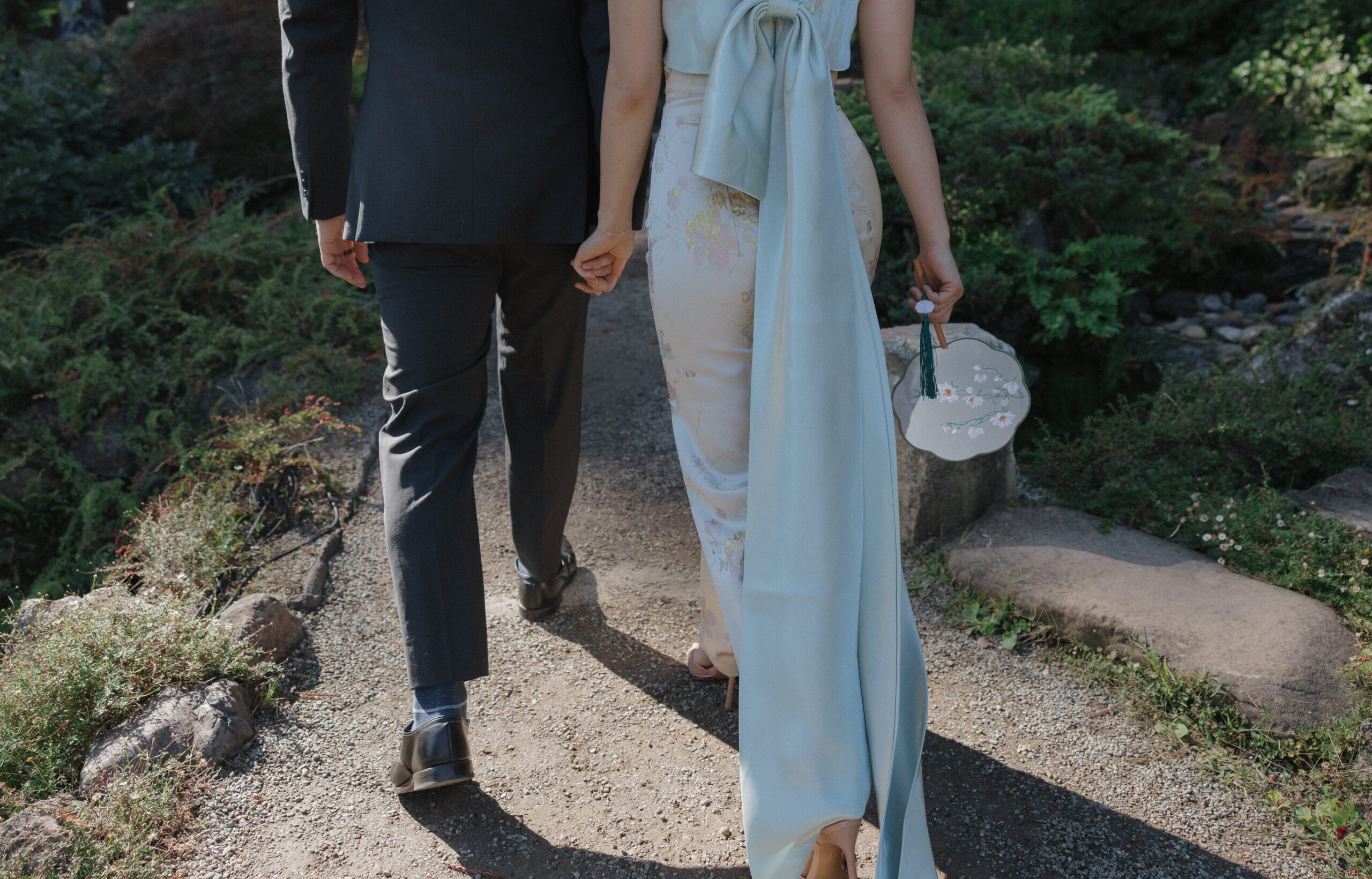 A photo of a couple walking away from the camera through a garden