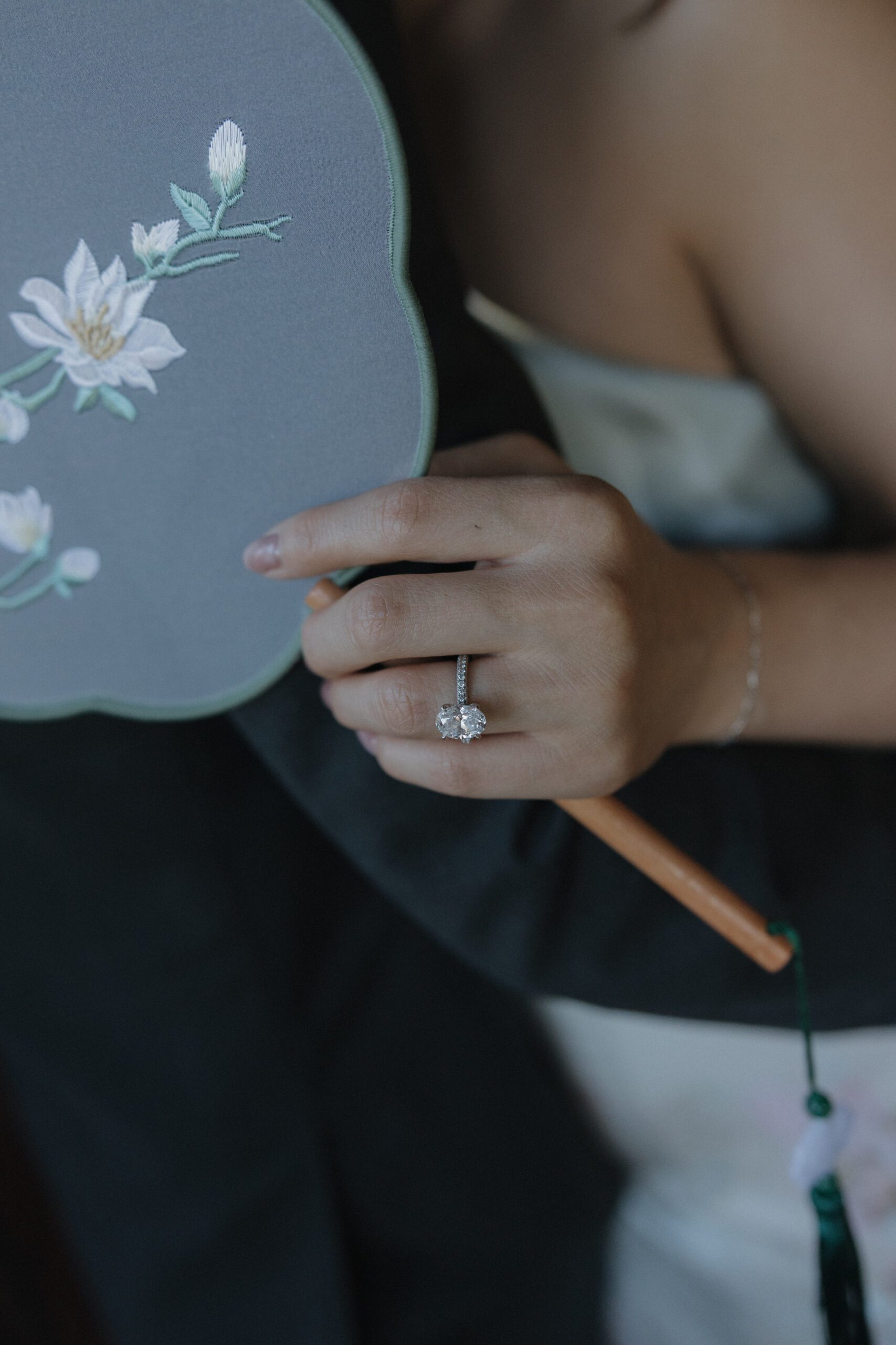 A woman's engagement ring while she's holding a flower-embroidered fan