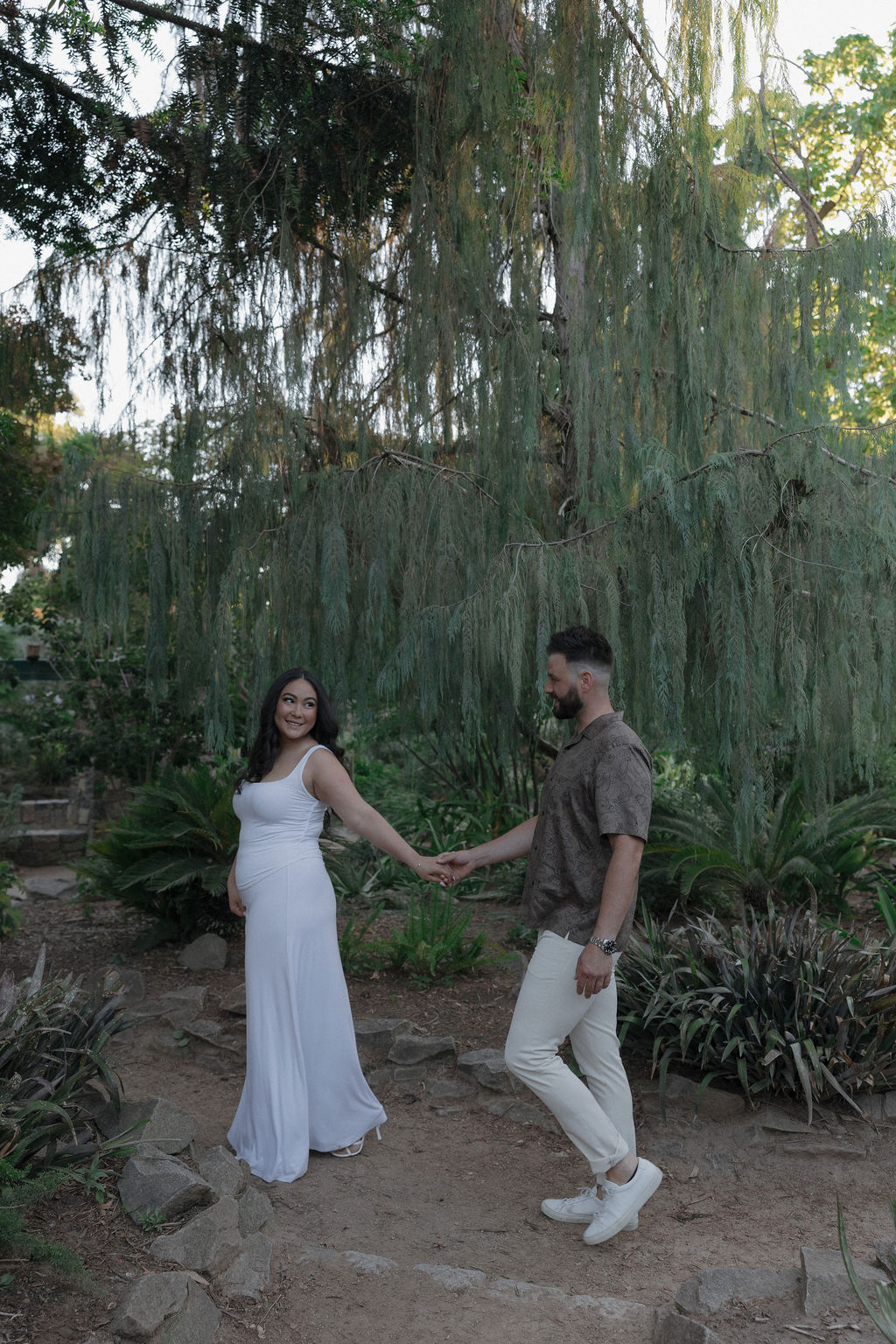 A couple walking through William Land Park in Sacramento holding hands for engagement photos