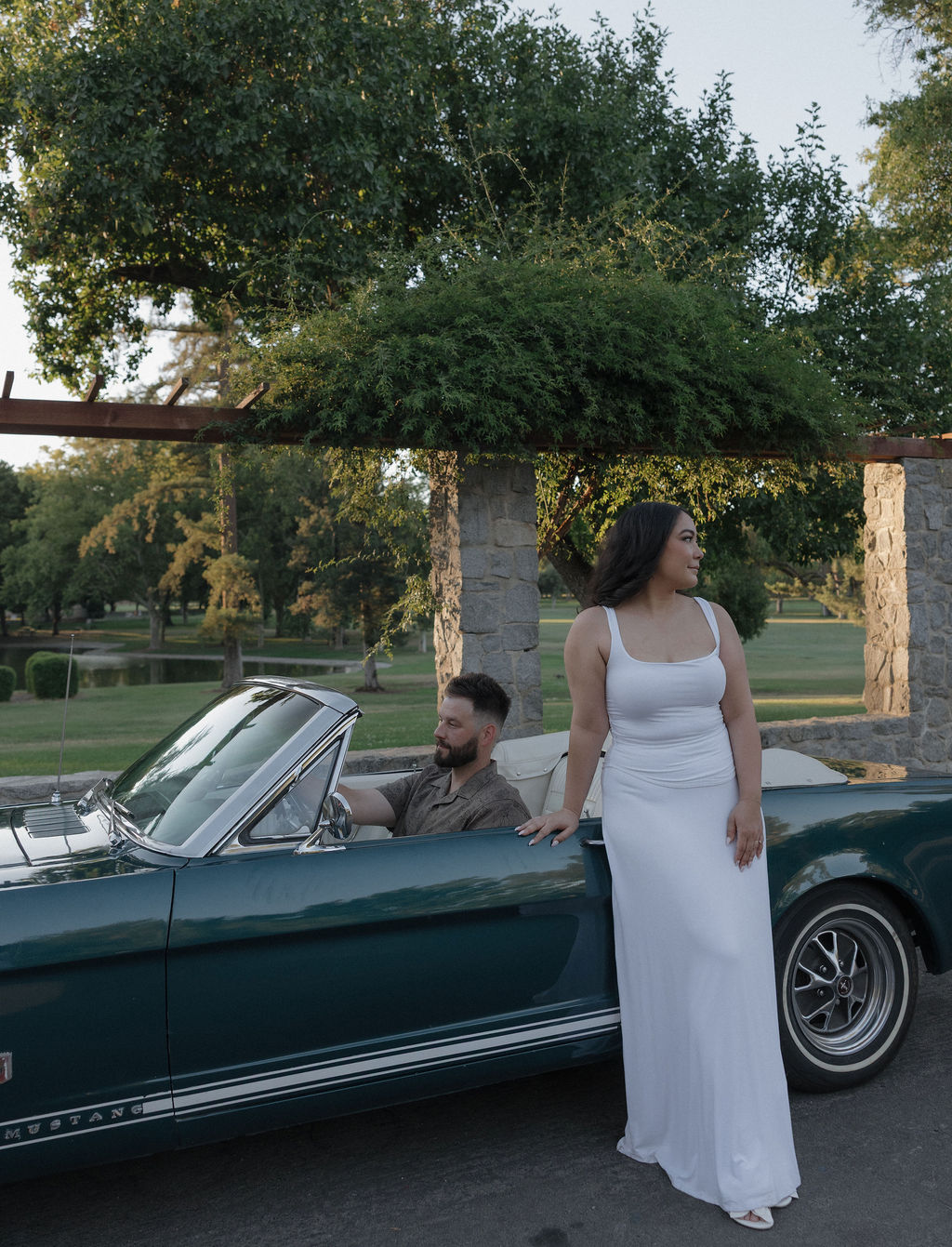 A woman standing beside her fiancé in a classic car for engagement photos