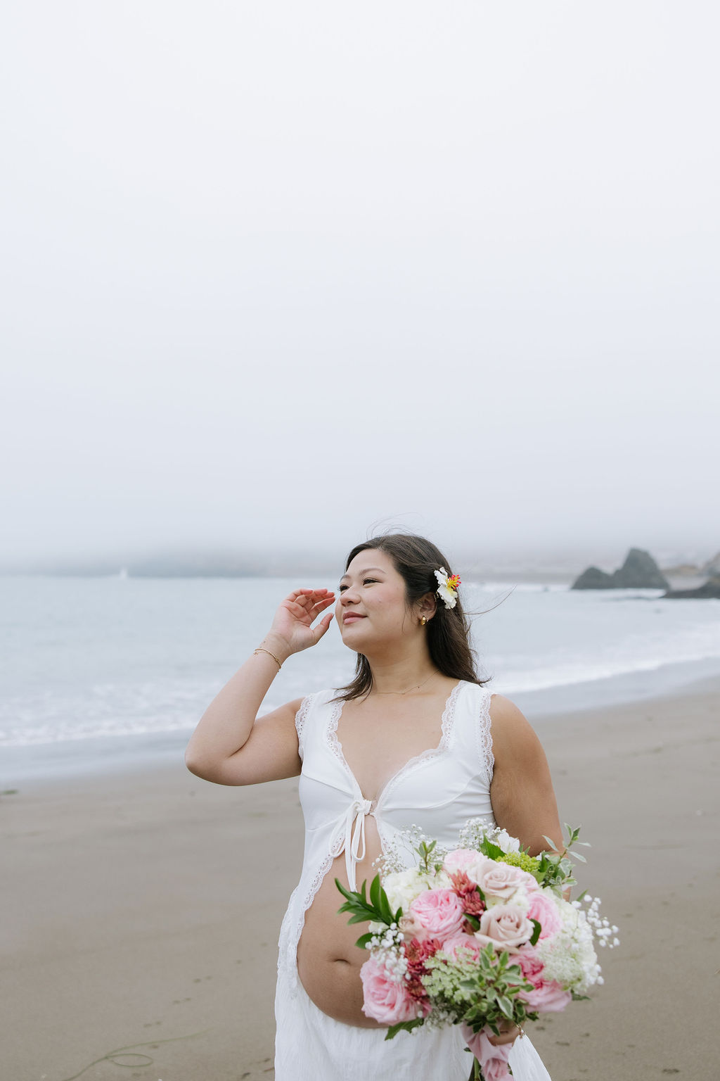 A woman holding a bouquet taking beach maternity photos