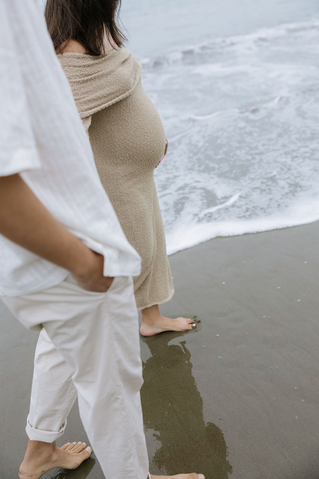 A couple walking through the ocean during beach maternity photos