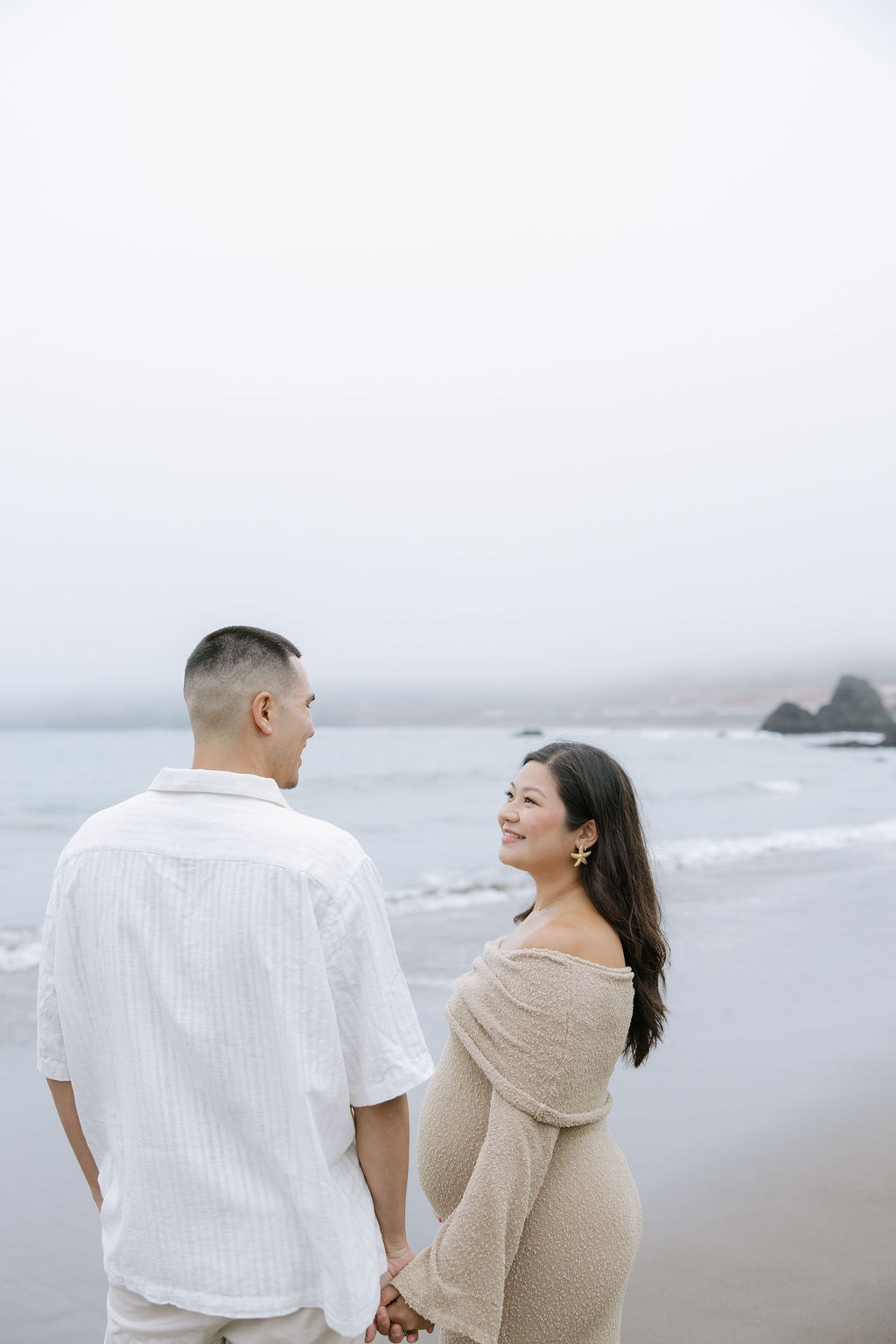 A couple holding hands on a beach during maternity photos