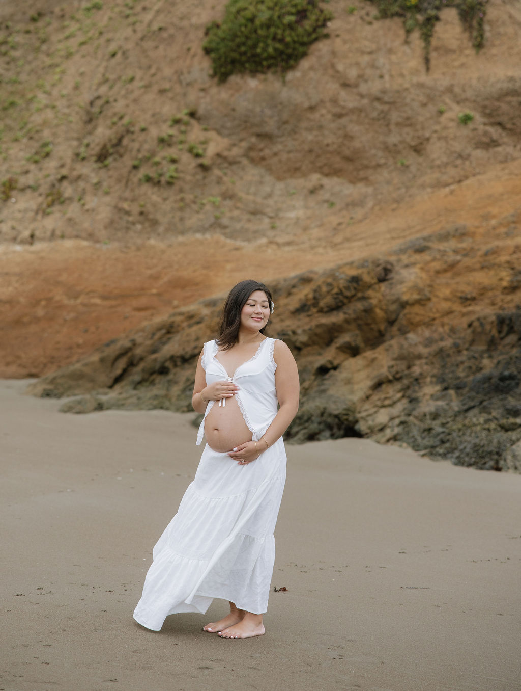 A woman posing for beach maternity photos in front of a rock formation