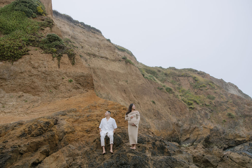 A couple posing on cliffs on a beach for a maternity photoshoot