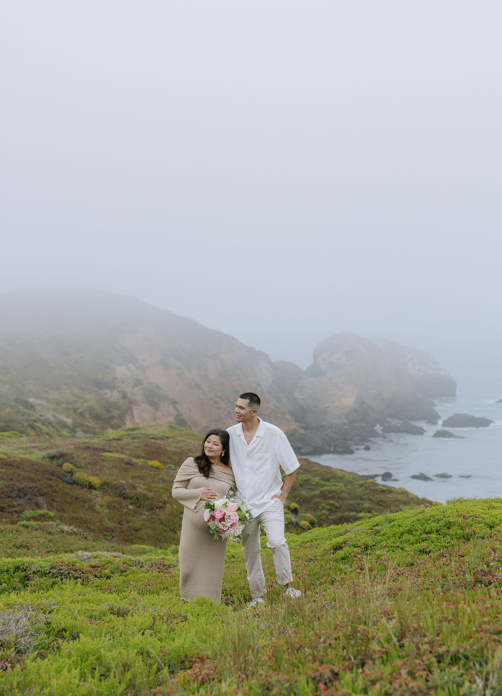 A couple posing on a beach cliff for maternity photos