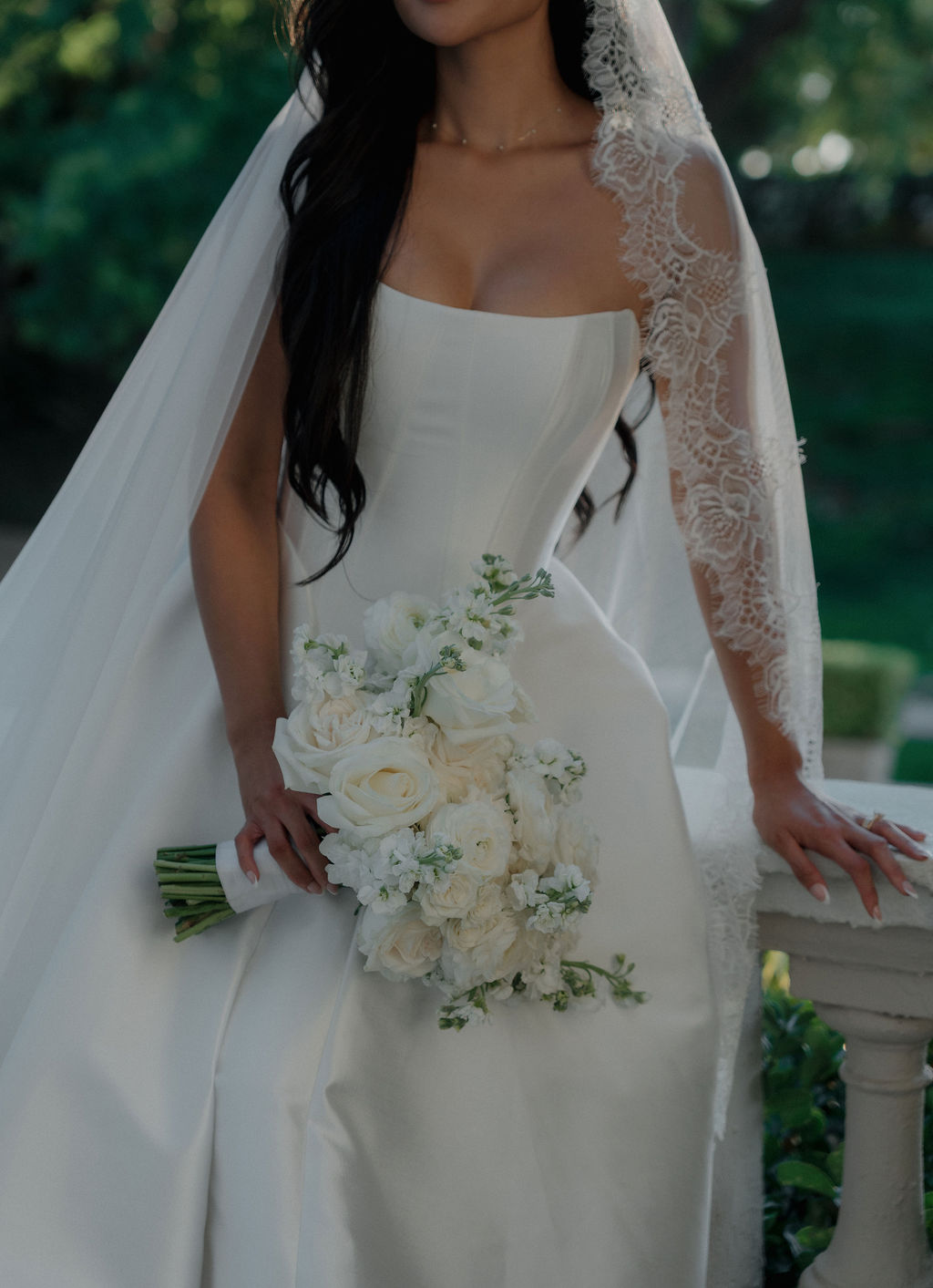 An up close photo of a brides simple wedding dress, lace veil, and bridal bouquet