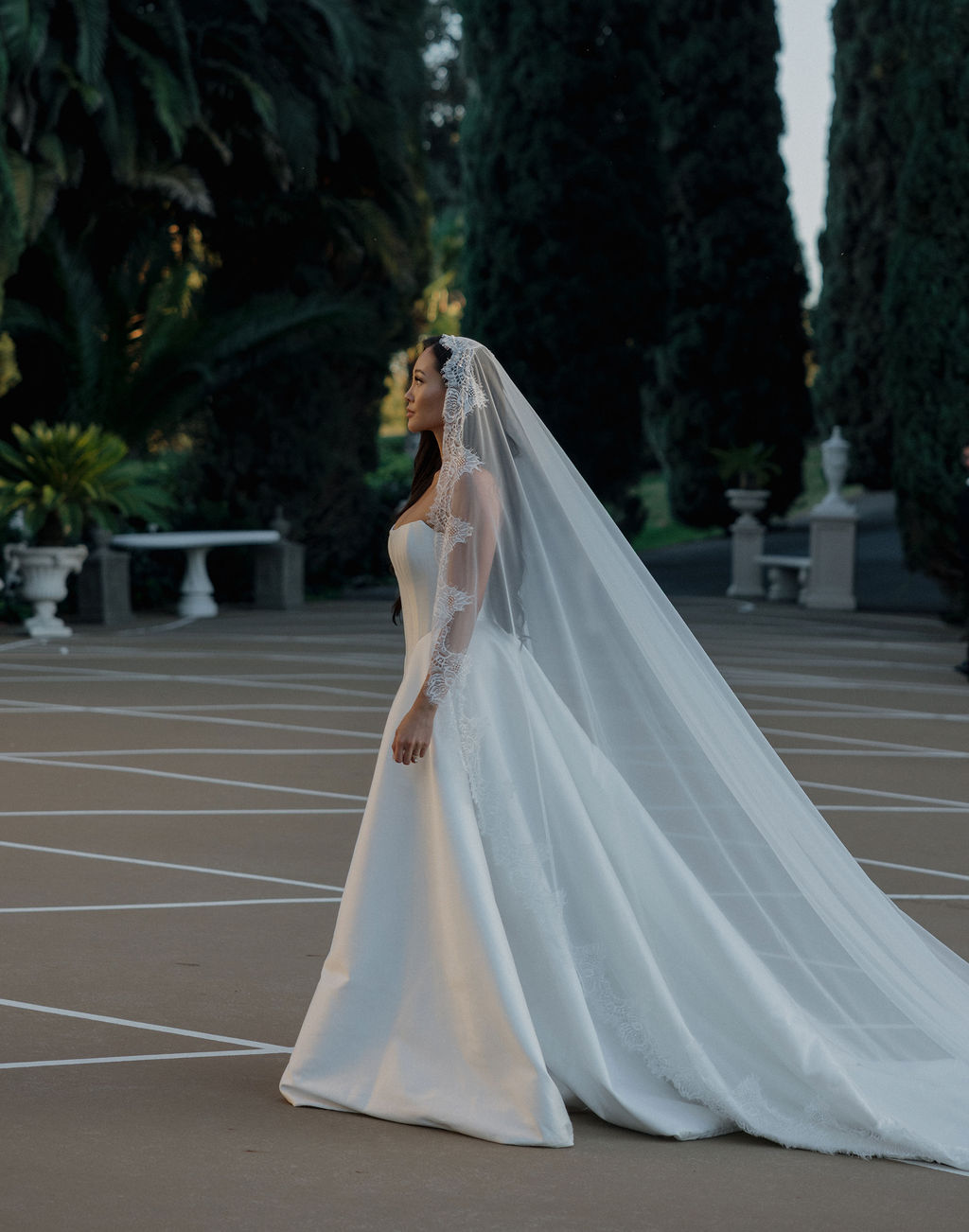 A bride waling in a simple elegant wedding dress with a mantilla veil across her Northern California wedding venue