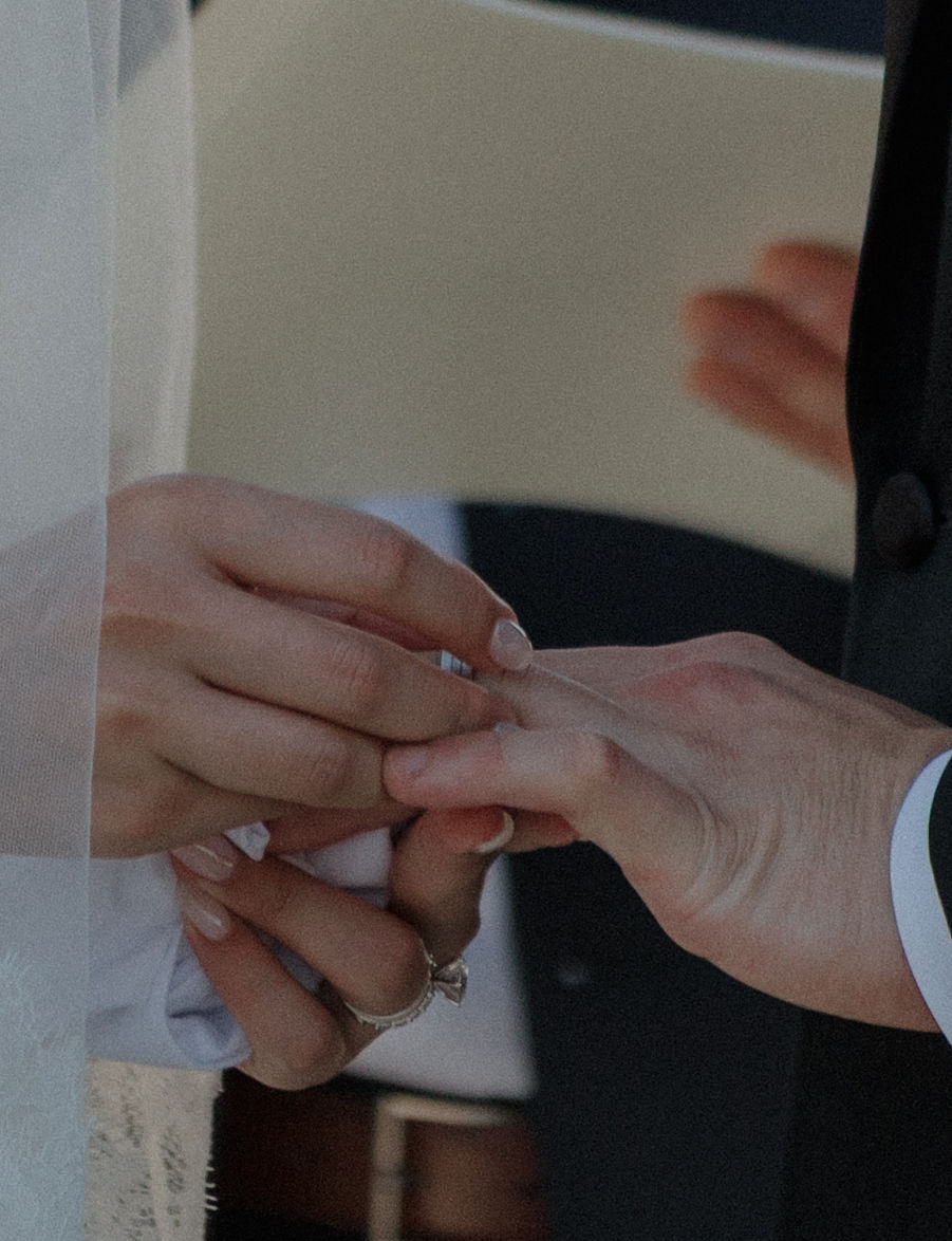 An up-close photo of a bride putting the ring on the groom's finger