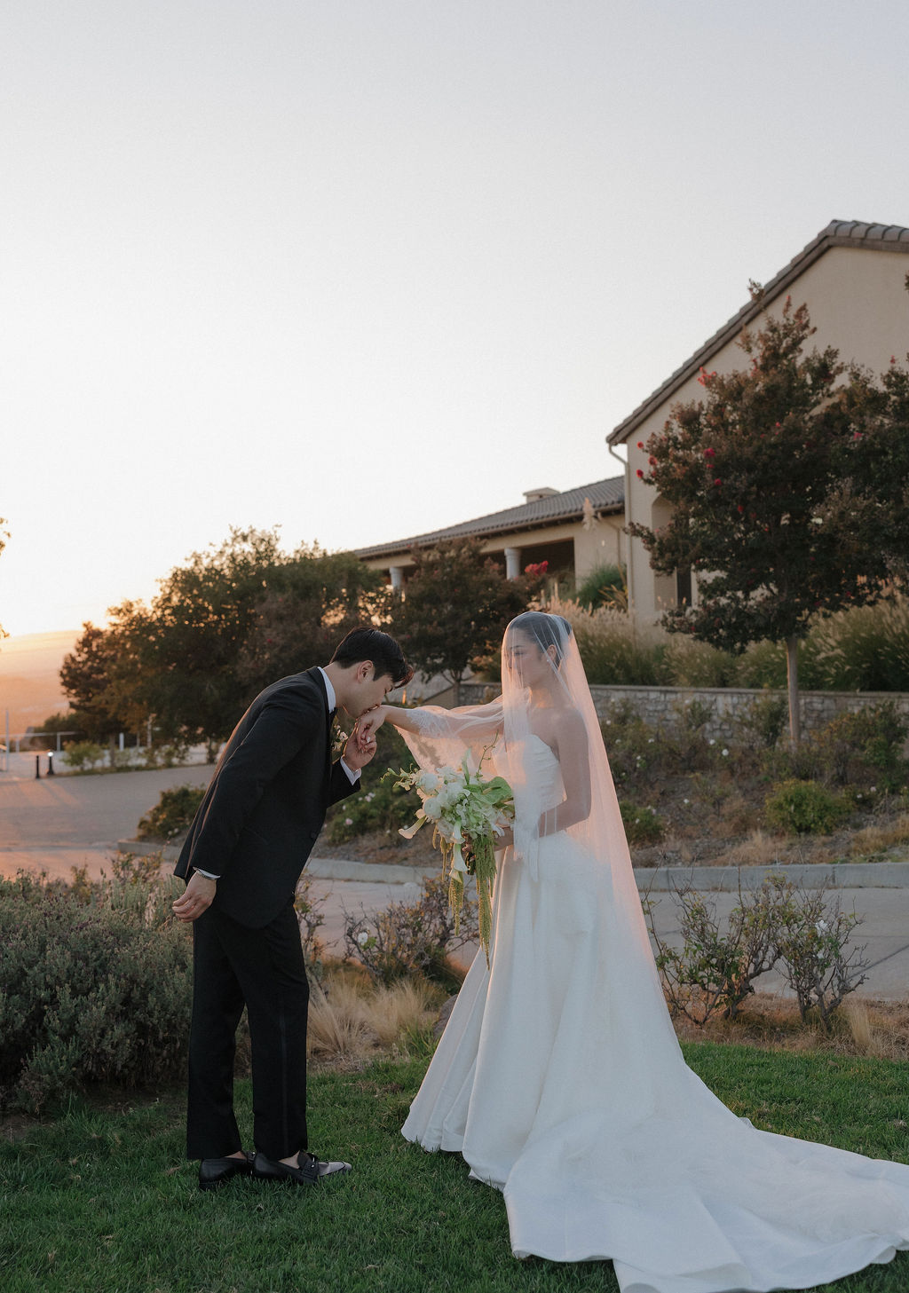 A bride and groom posing for wedding photos with a groom kissing bride's hand