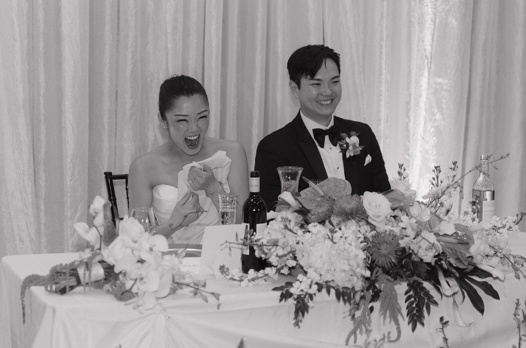 A candid wedding photo of a bride and groom laughing at a wedding reception