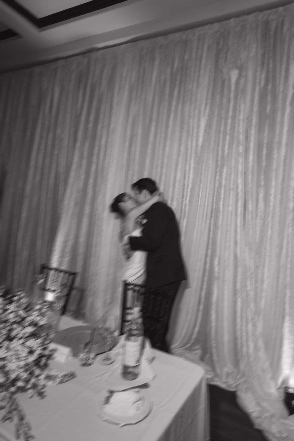 A blurry candid photo of a bride and groom kissing at their sweetheart table
