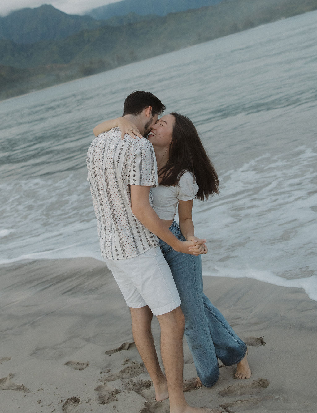 A couple taking engagement photos on the beach on Hanalei Bay with a Kauai photographer
