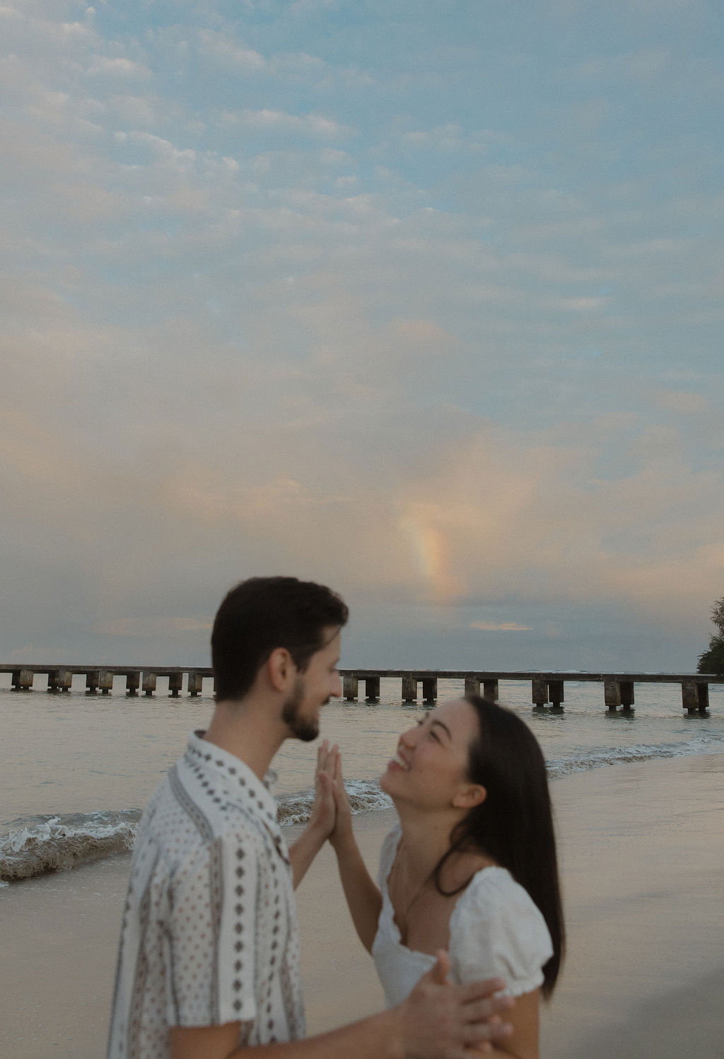 A couple holding hands in front of a rainbow on Hanalei Bay Pier