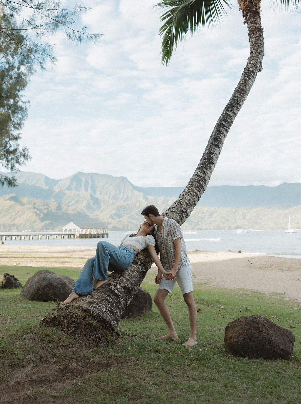 A girl sitting on a palm tree with her fiancé standing beside her