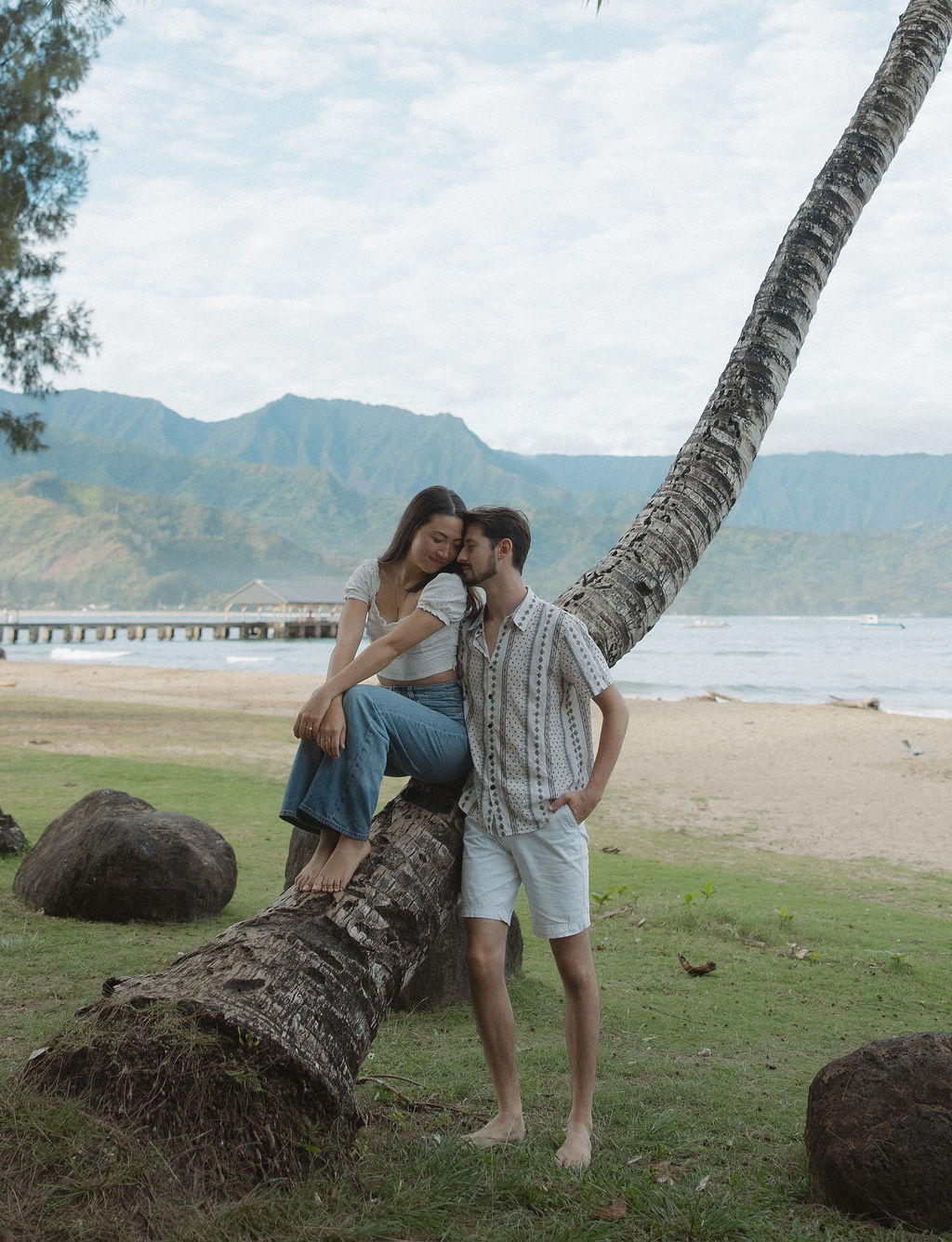 A girl sitting on a palm tree with her fiancé standing beside her