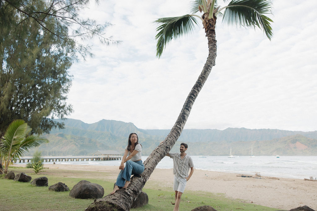 A girl sitting on a palm tree beside her fiancee at Hanalei Bay