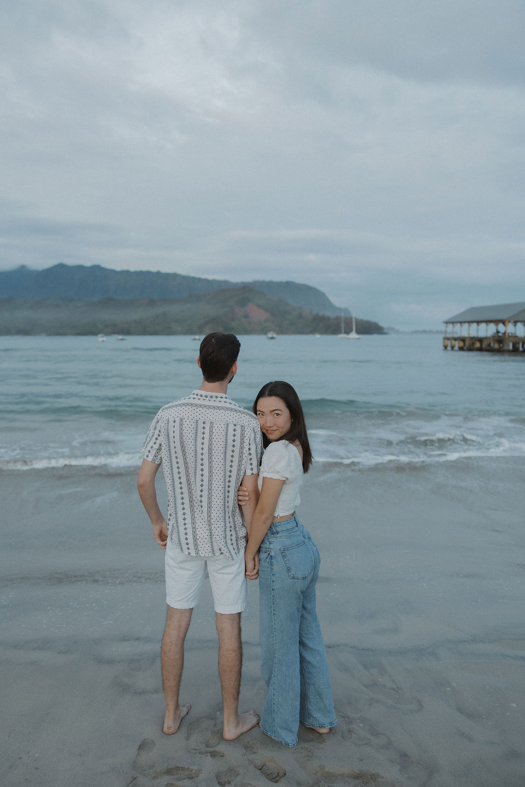 A couple standing on the beach facing the ocean