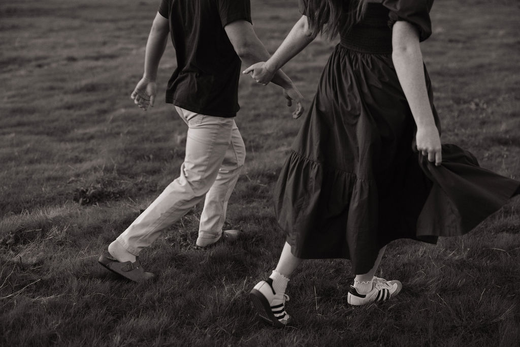 A couple walking through a field hand-in-hand showing engagement photo ideas