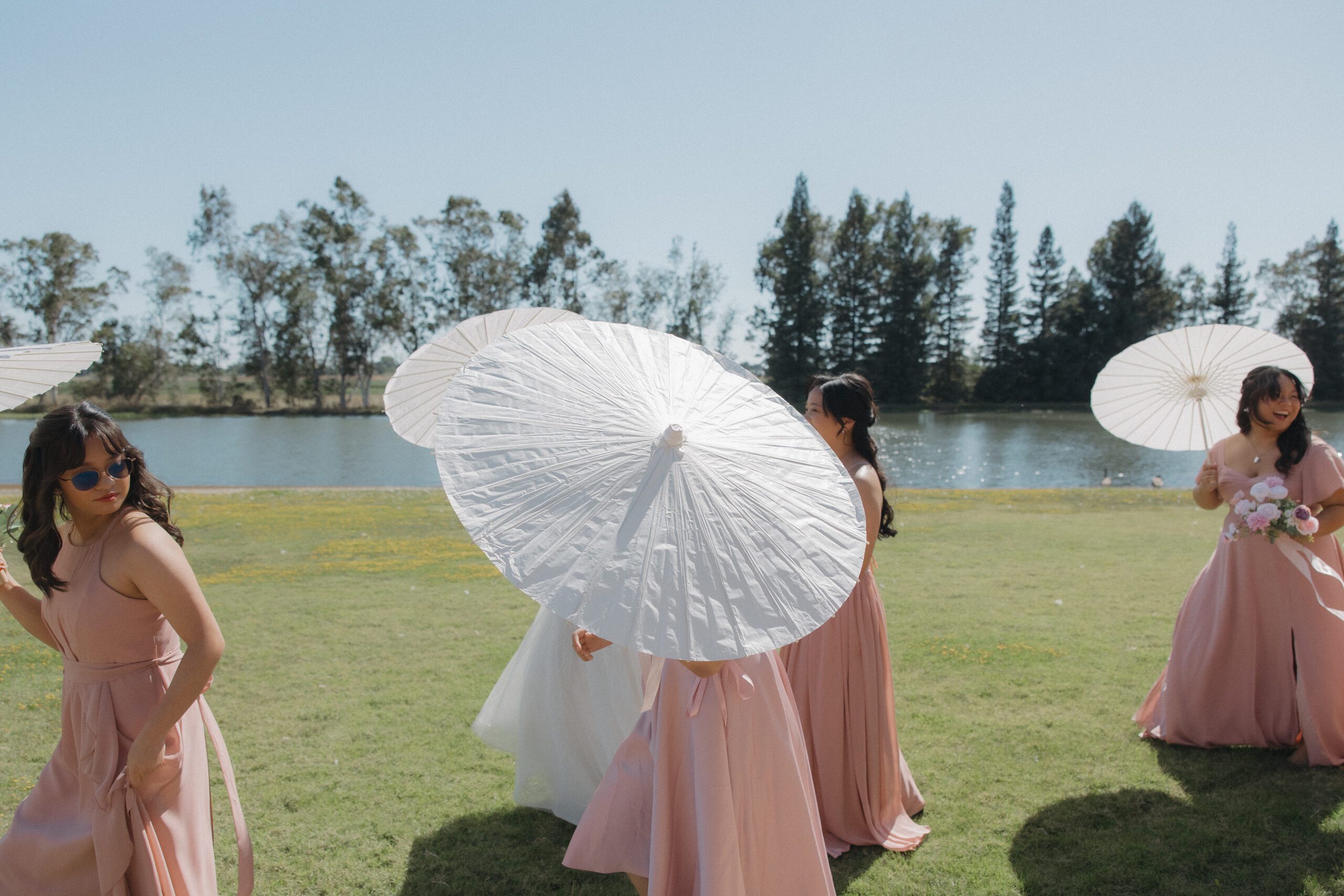 Bridesmaids walking across a Sacramento wedding venue with parasols