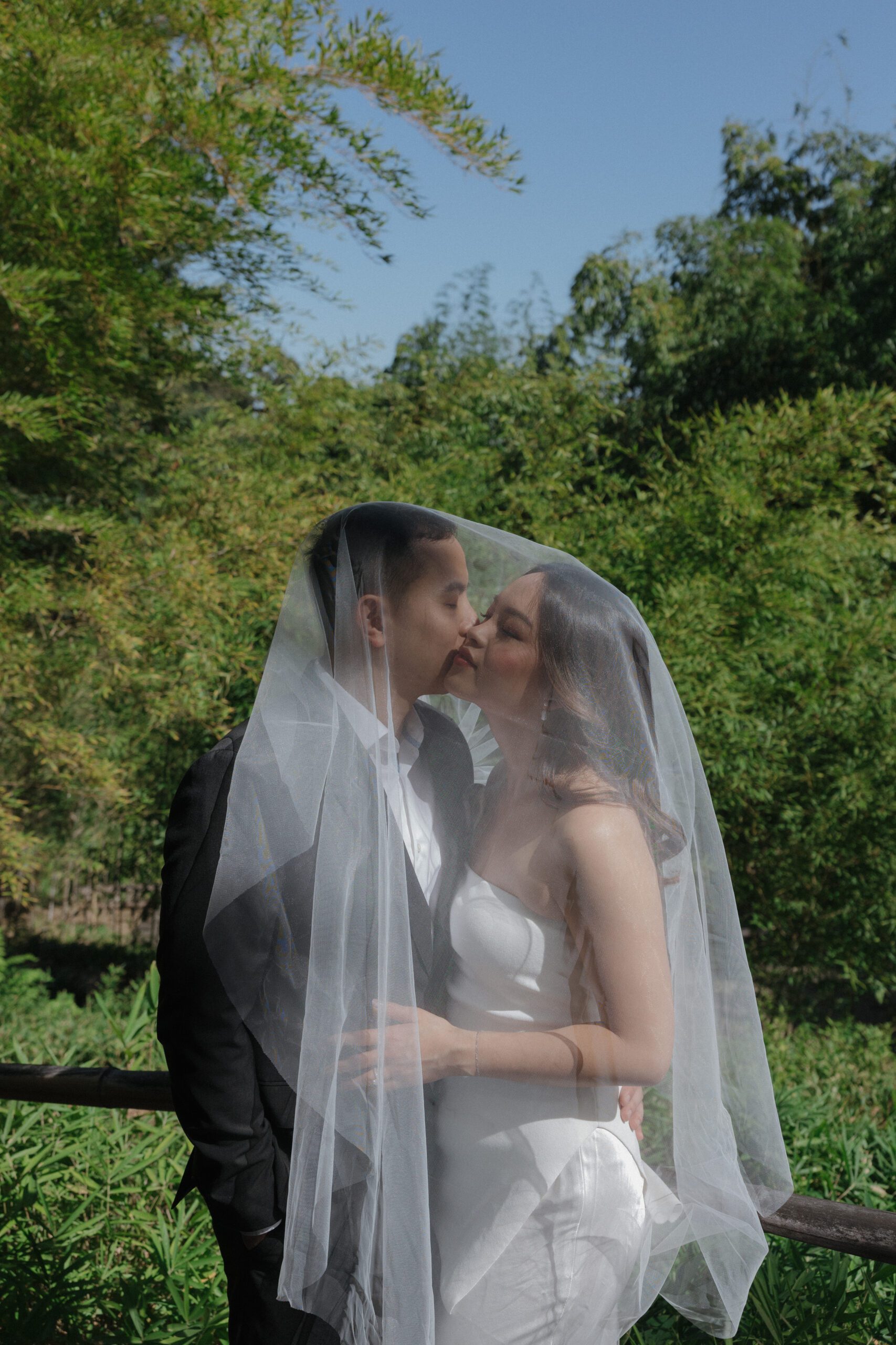 A groom kissing a bride on the cheek underneath a wedding veil