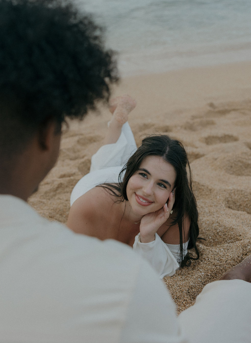 A bride lying on the beach, looking up at a groom