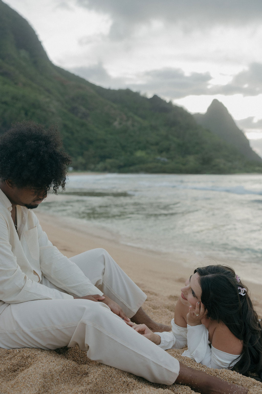 A bride lying on the beach, looking up at a groom