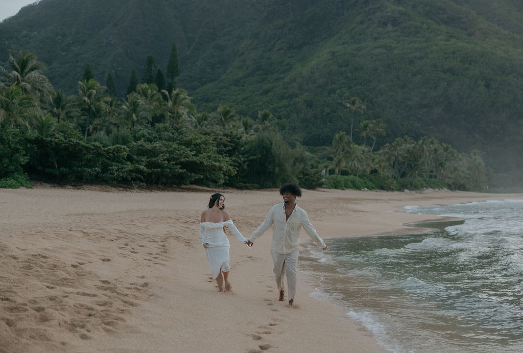 A bride and groom running on the beach after their Hawaii elopement