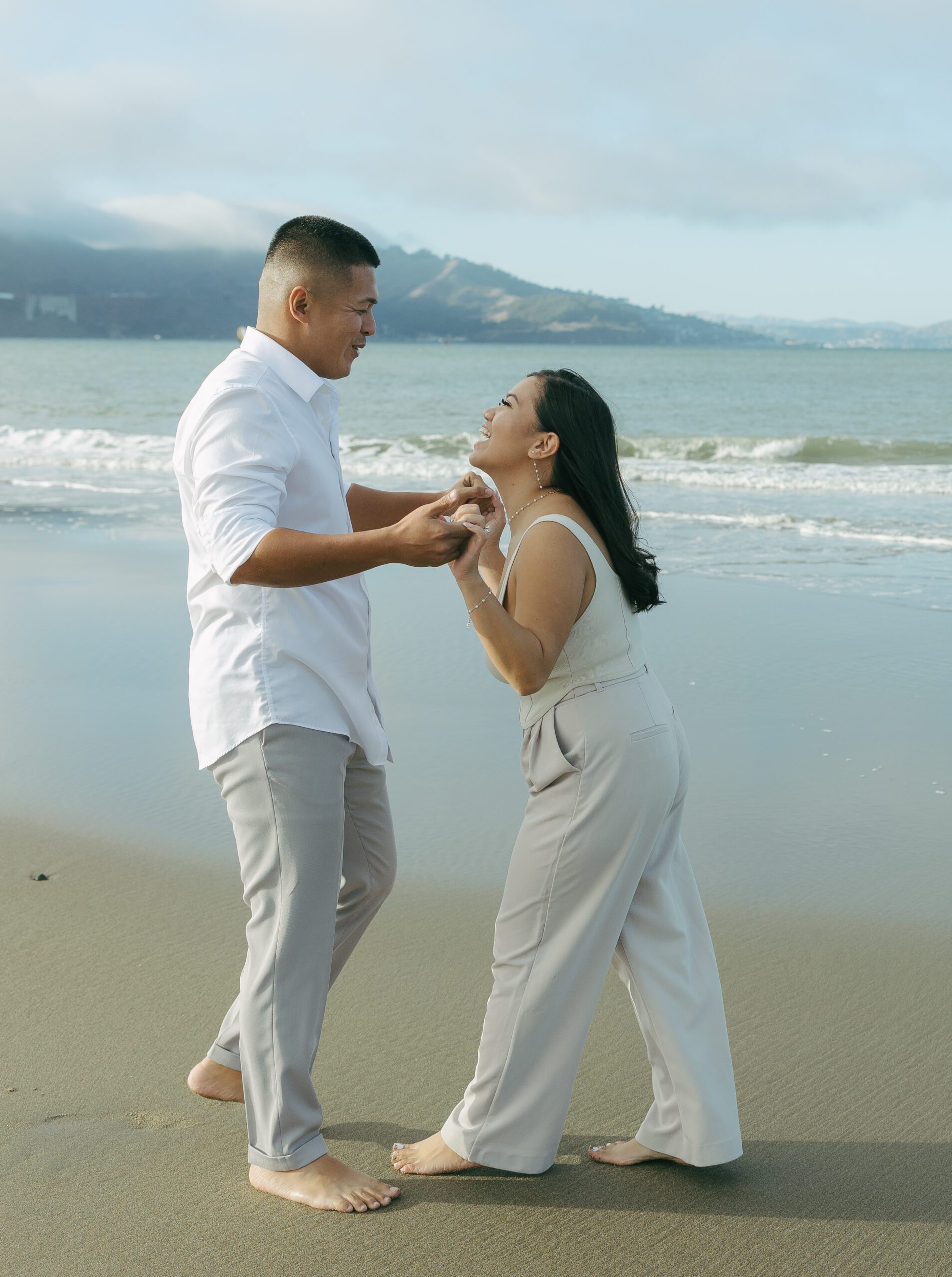 A couple taking beach engagement photos in casual outfits
